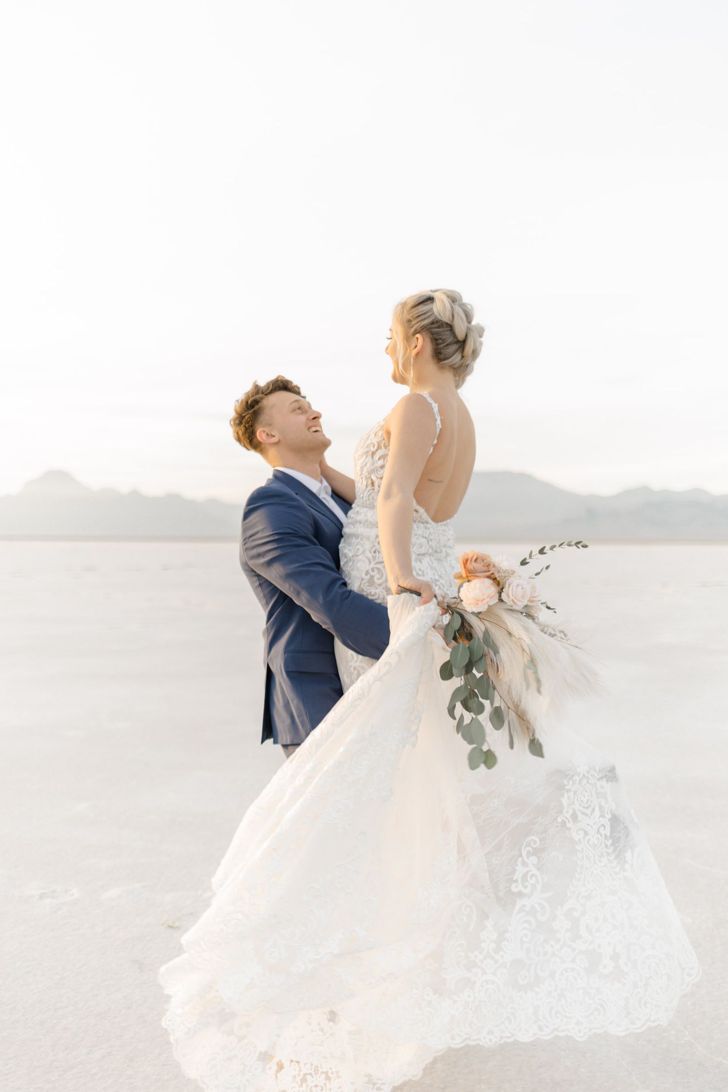 Bride and groom share a romantic dance pose against a bright desert landscape backdrop.
