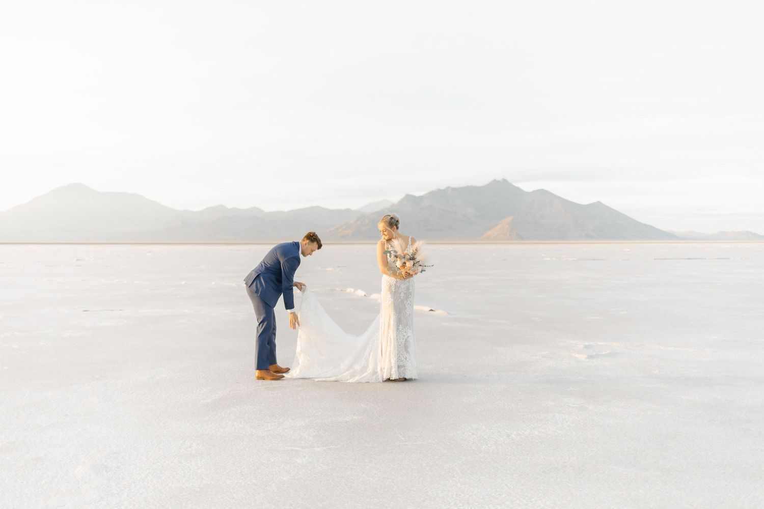 A couple takes romantic wedding photos on the vast white salt flats under a cloudy sky.