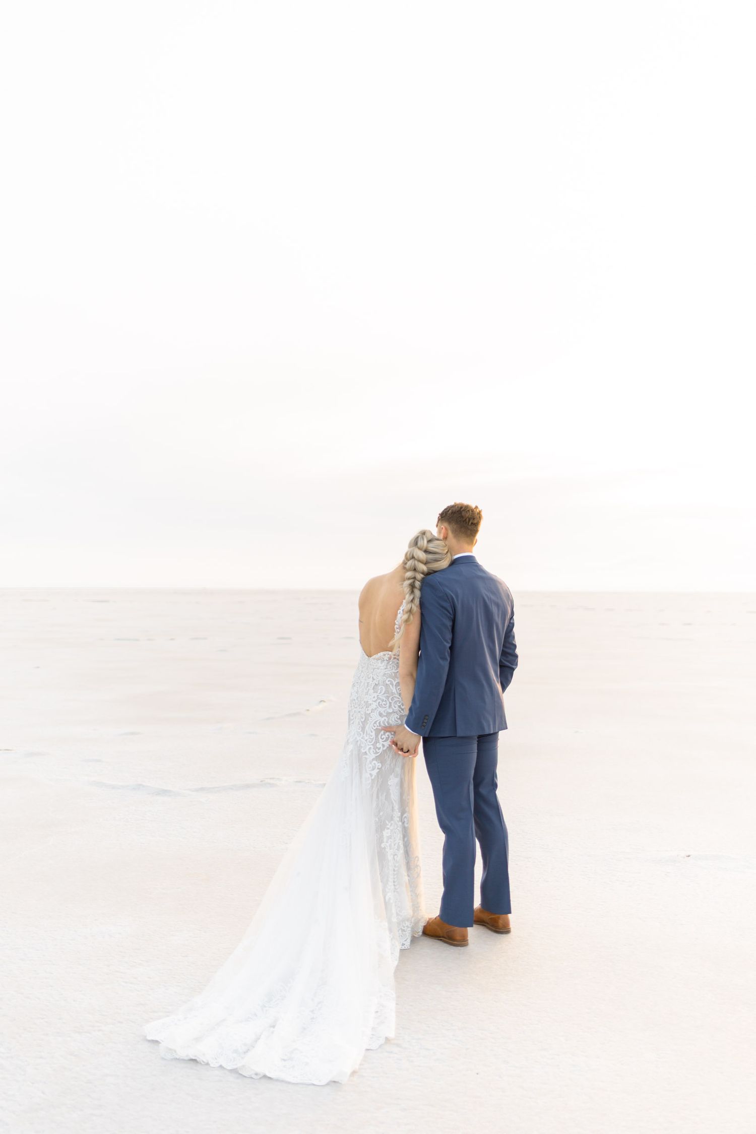 A romantic wedding couple stands together on a bright white surface in elegant wedding attire.