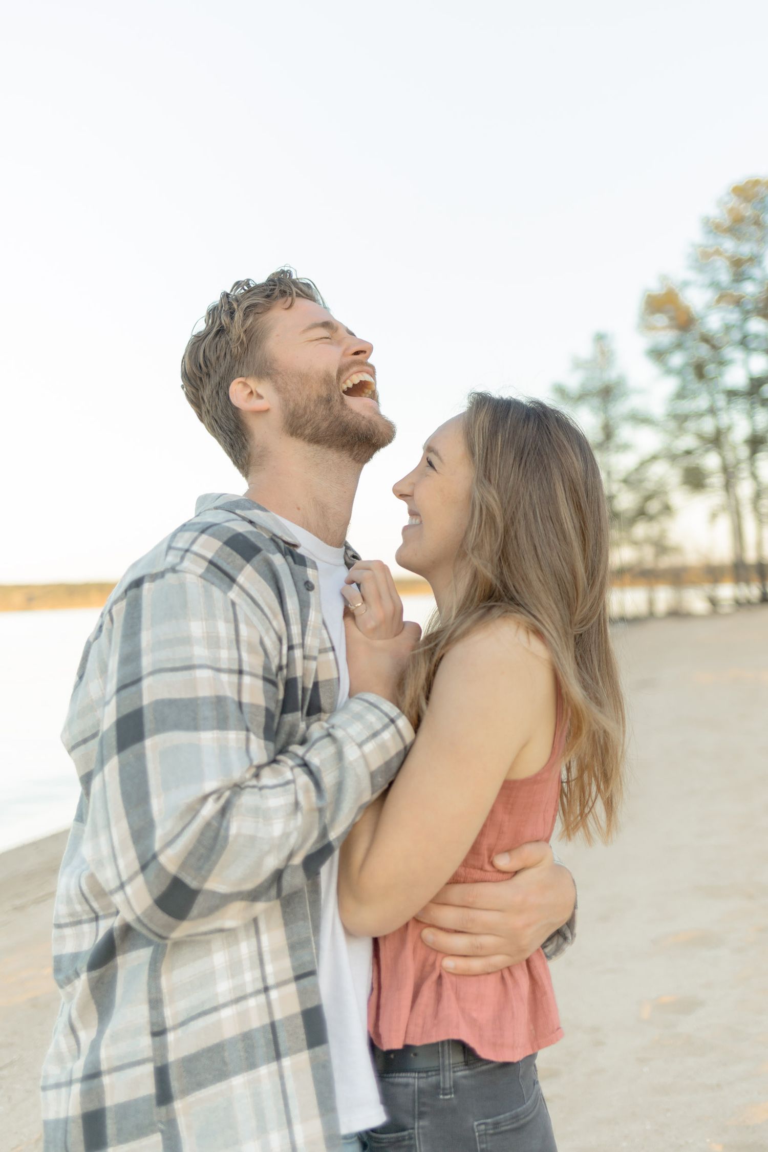 Joyful couple sharing laughter while embracing on a sandy beach during sunset in Raleigh, North Carolina.