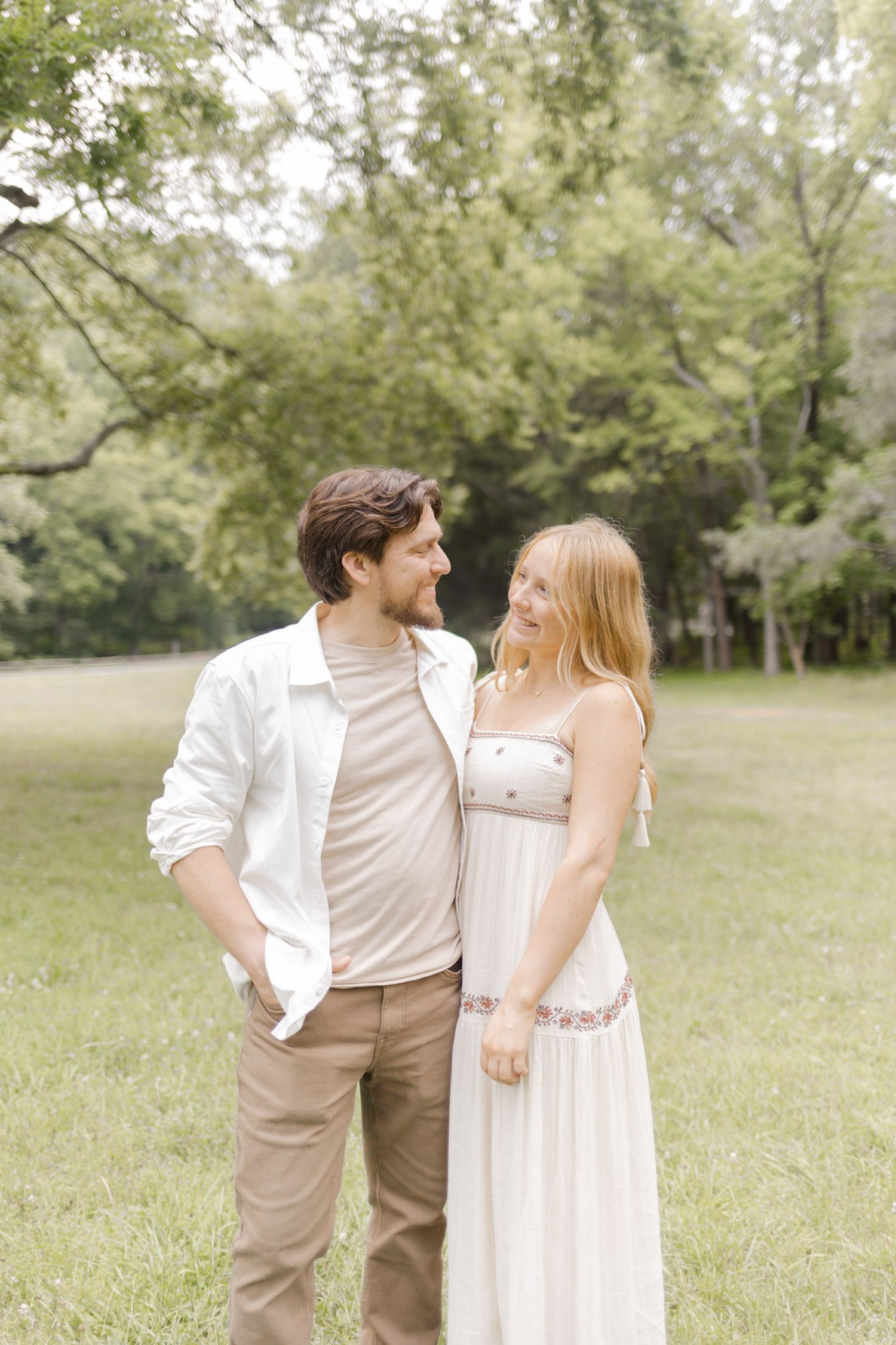 A couple shares tender moments together in a sun-drenched field wearing coordinating neutral outfits during photoshoot in Durham, NC.