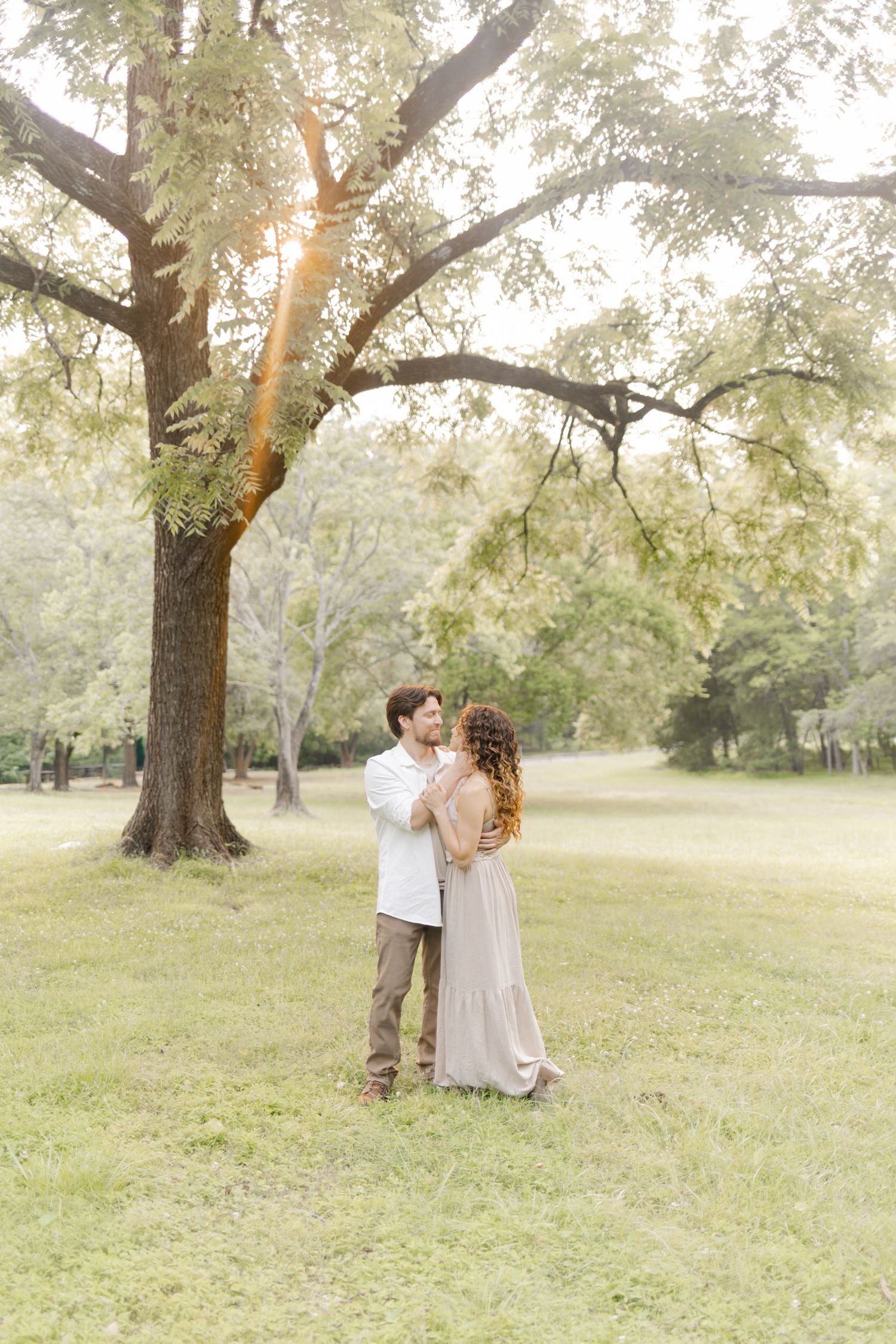 Romantic couple shares tender moments in a sun-dappled park setting during photoshoot with Kinsley Nicole Photography.
