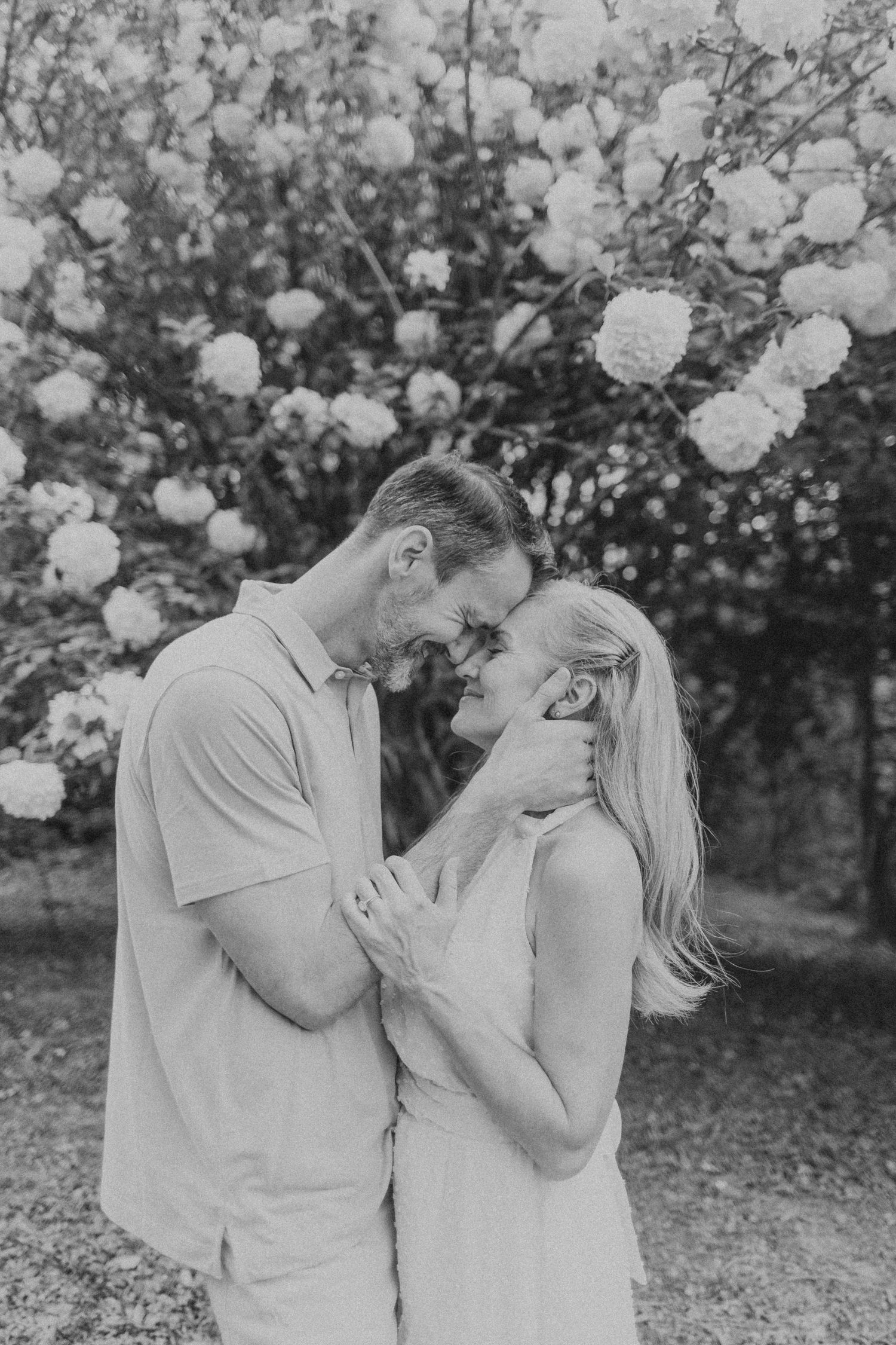 Romantic couple sharing intimate moments among blooming white flowers in black and white.