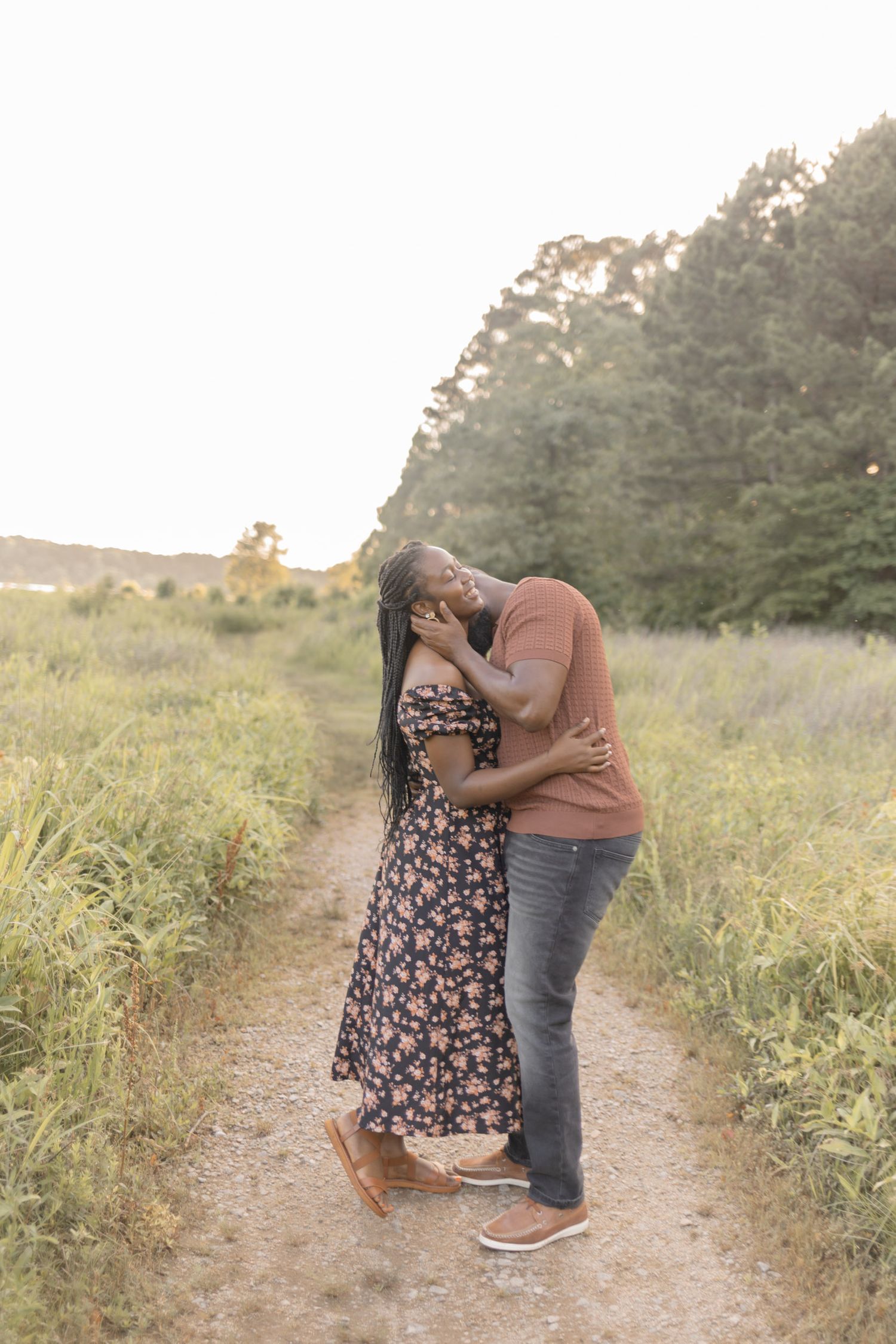 A couple shares a tender kiss on a rustic path in a lush meadow bathed in warm sunset light.