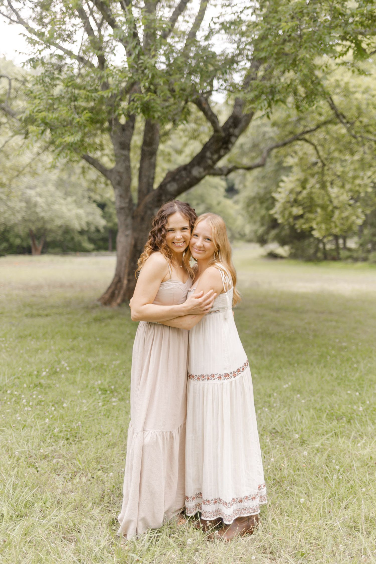 Two people share an intimate moment in a grassy field while wearing flowing cream-colored dresses during photoshoot in Durham, NC.