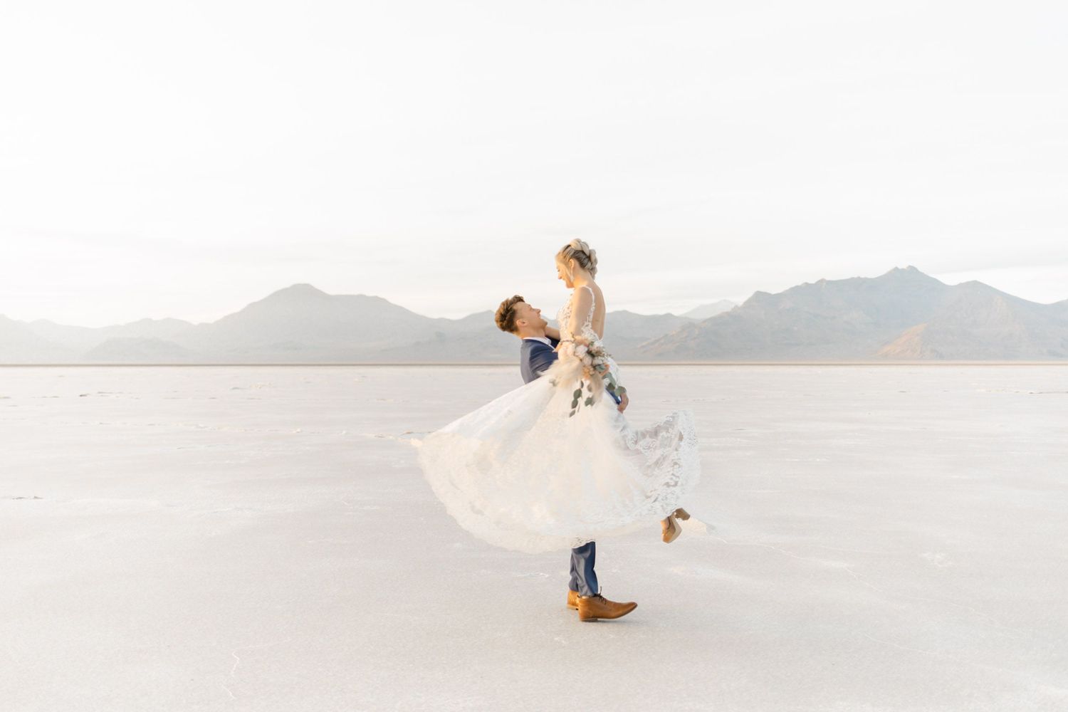 A bride and groom twirl joyfully on the pristine white salt flats with mountains visible in the distance.