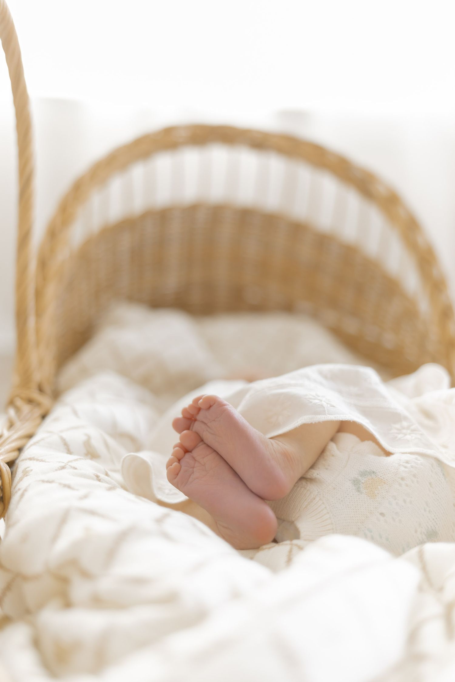 Tiny newborn baby feet resting in a wicker Moses basket with white bedding.