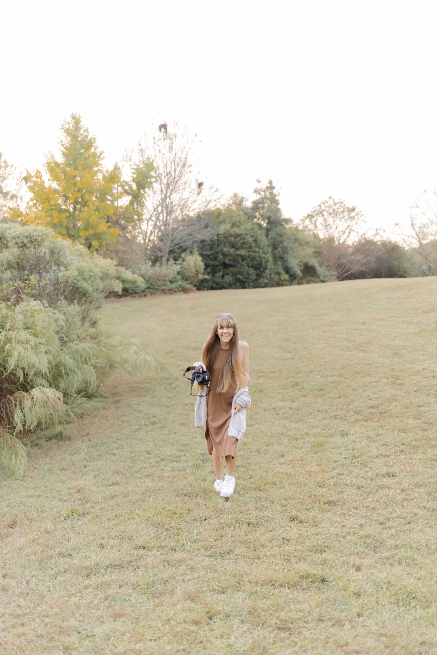 A person wearing white sneakers and casual clothing photographs on a grassy slope.