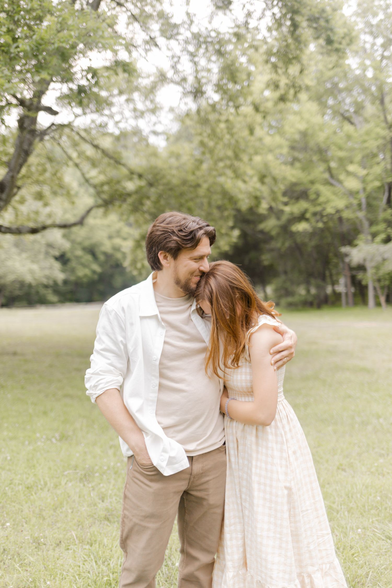 A tender moment between a couple in neutral-toned clothing against a backdrop of trees during photoshoot in Durham, NC.