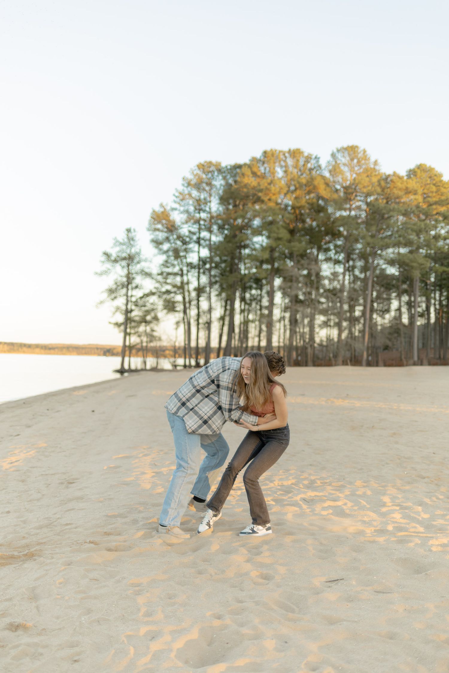 Two people playing and laughing together on a beach with pine trees at sunset during their couples lifestyle photoshoot in Raleigh.