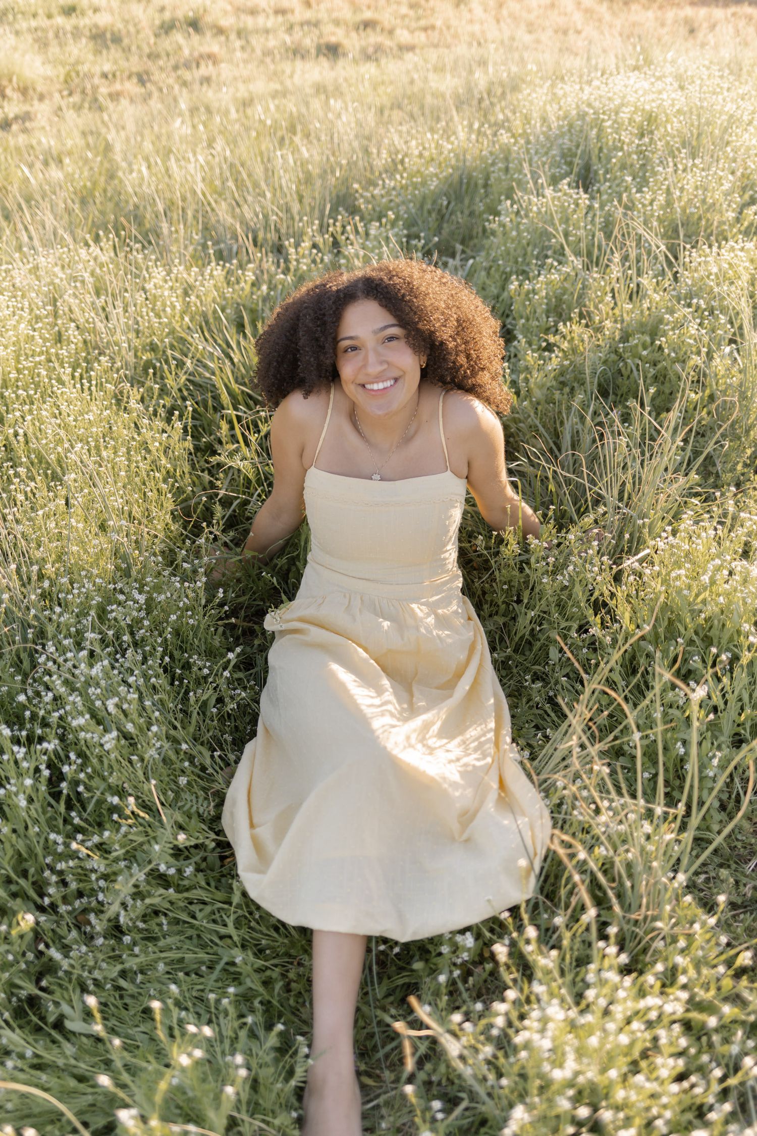 Happy woman in yellow sundress walking through wildflower meadow in bright natural sunlight.