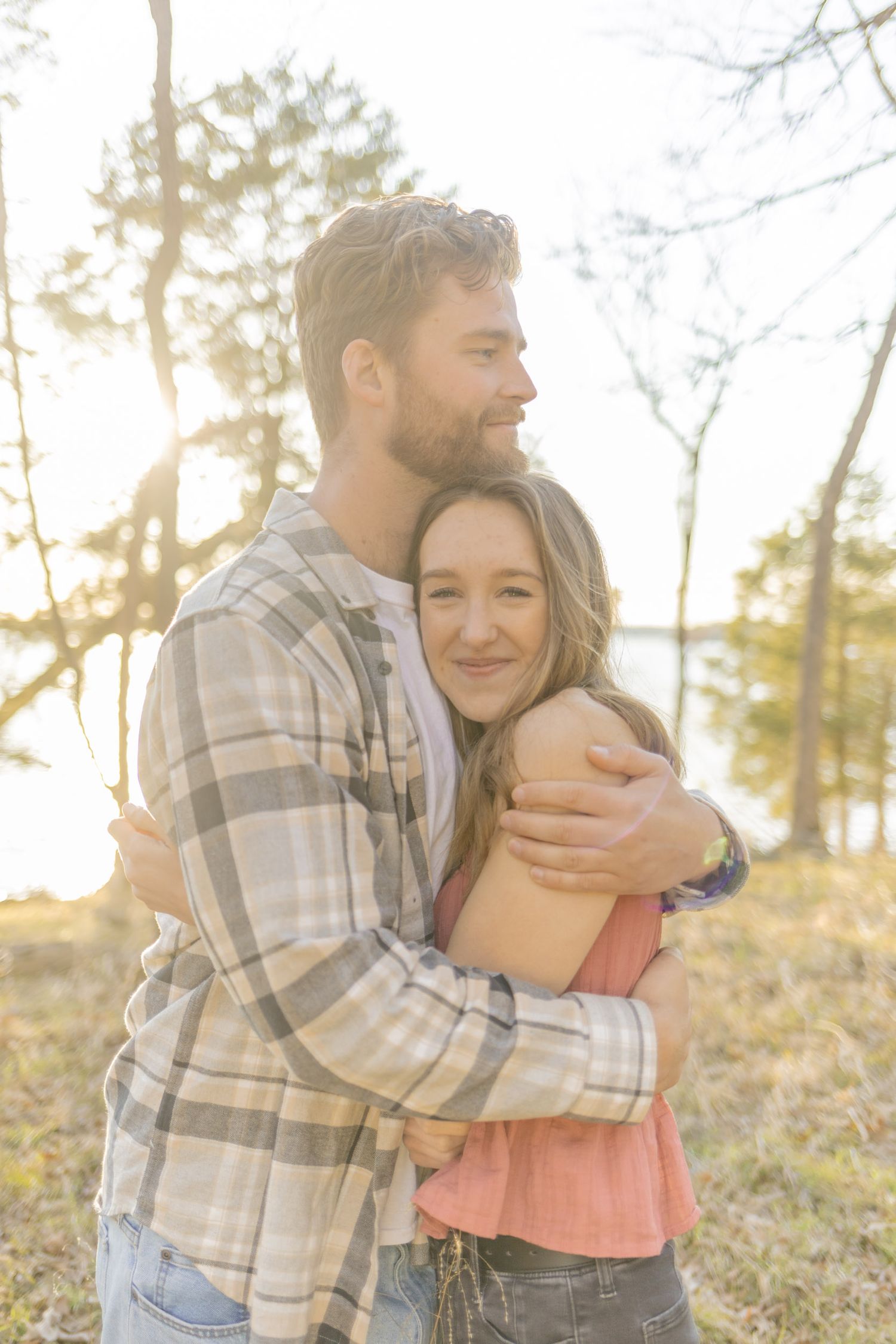 Affectionate embrace captured in sunlit forest setting during golden hour in Raleigh, North Carolina.