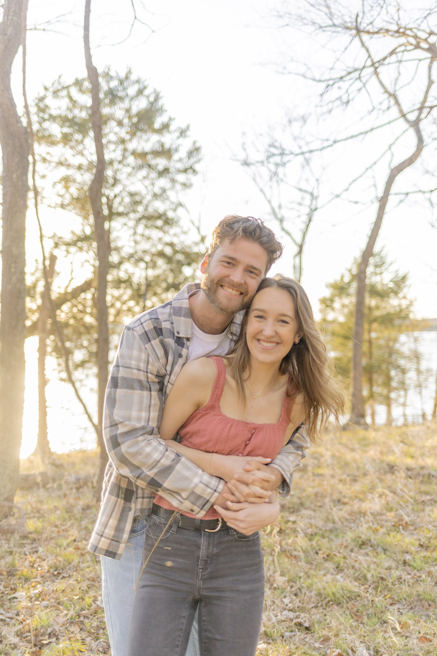 Joyful couple sharing laughter in sunlit wooded setting during golden hour in Raleigh, North Carolina.