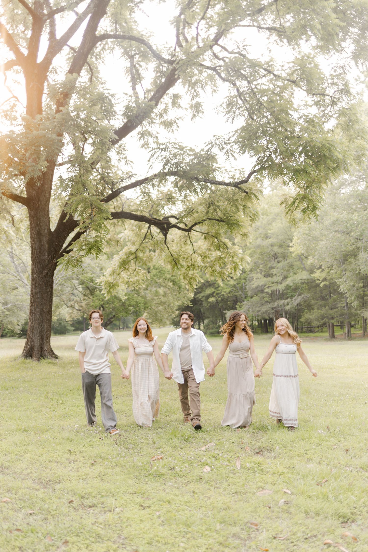 Five people in coordinated neutral outfits walk together holding hands across a grassy park during photoshoot with Kinsley Nicole Photo