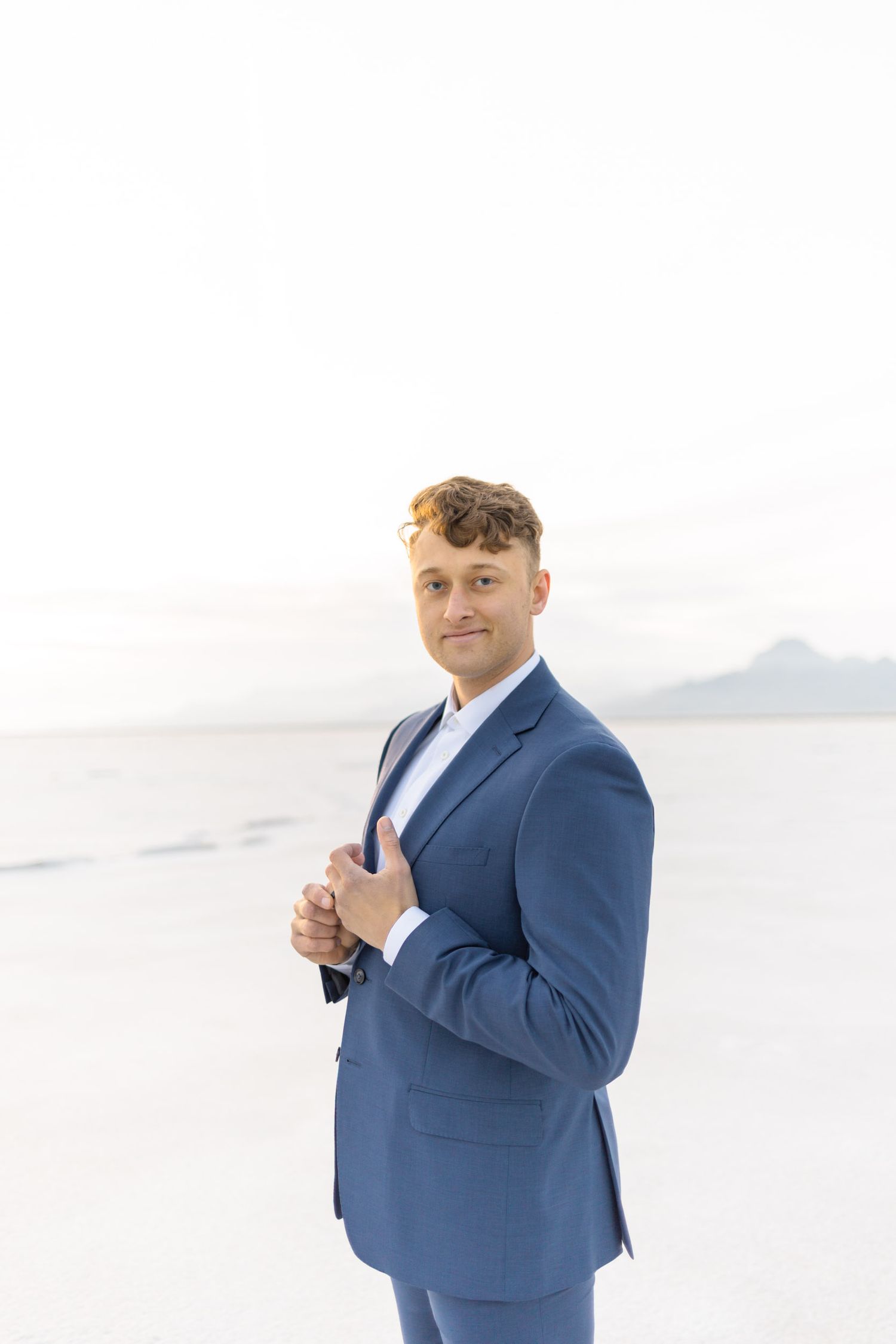 Person in navy blue suit stands confidently against white background making hand gestures.