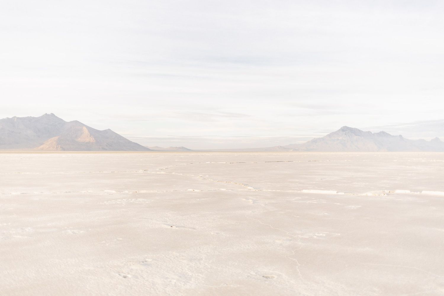 A vast salt flat desert landscape stretches towards distant mountains under a cloudy sky.