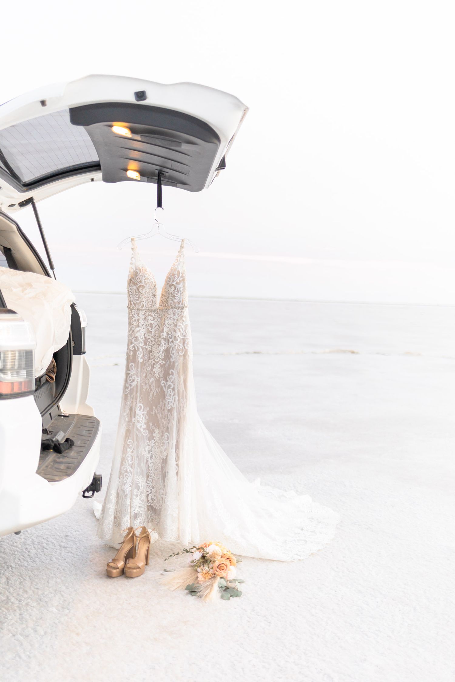 Wedding dress and bouquet details against stark white salt flat landscape.