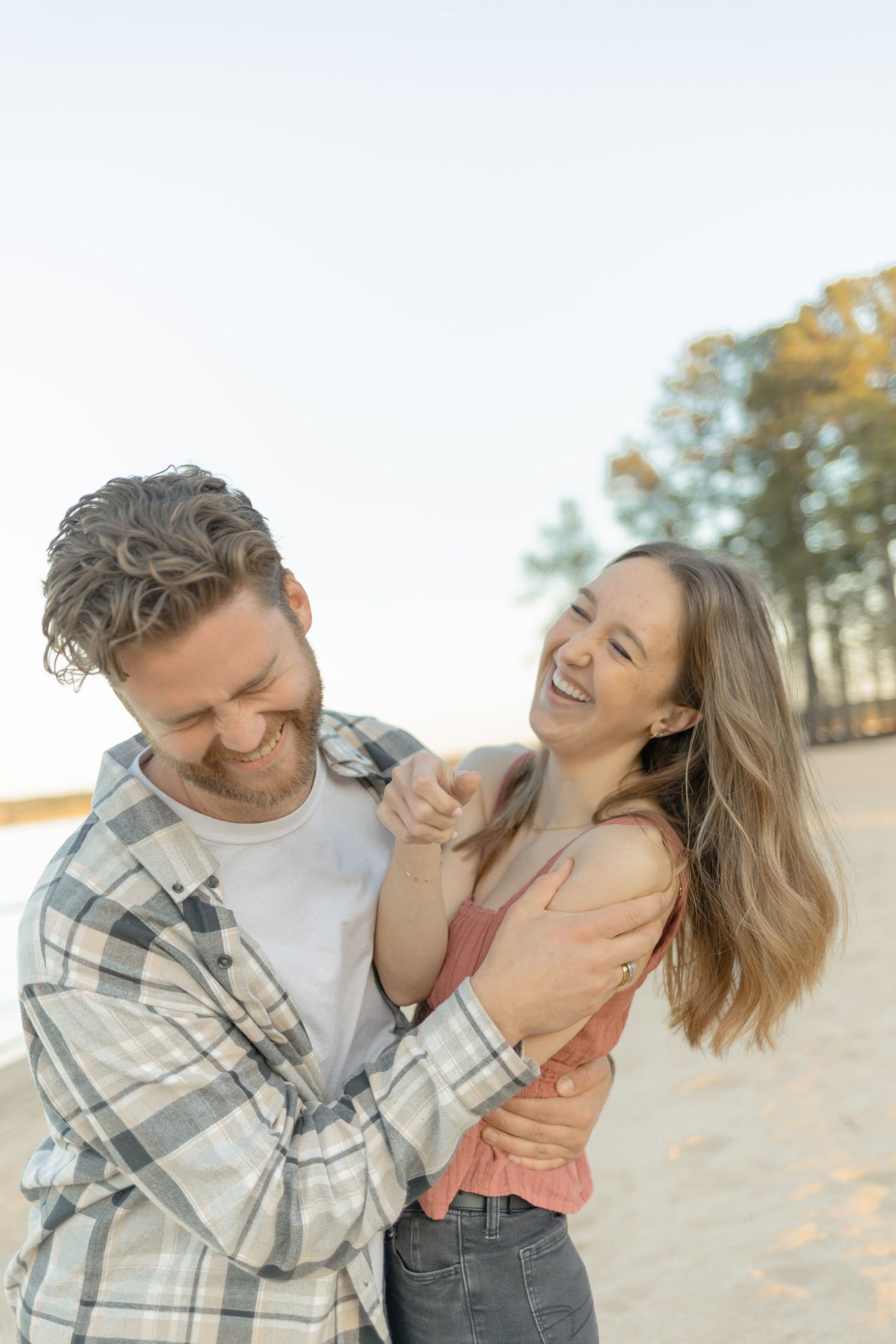 Candid moment of a couple laughing and embracing on a beach with natural lighting in Raleigh, North Carolina.