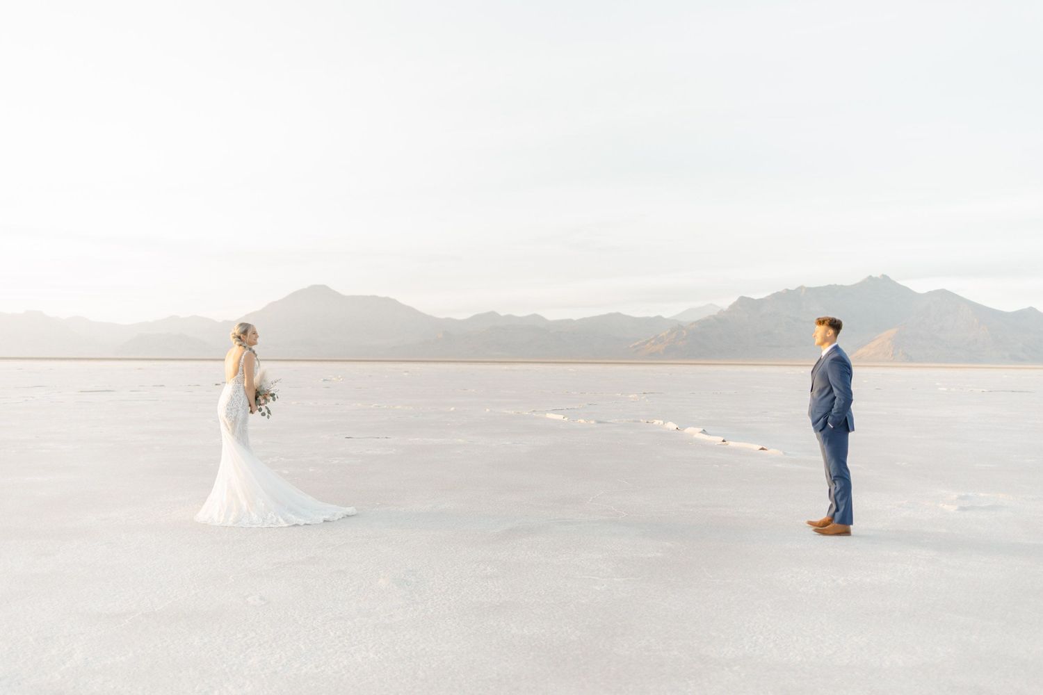 Wide landscape shot of couple on minimalist white salt flats with distant mountains.