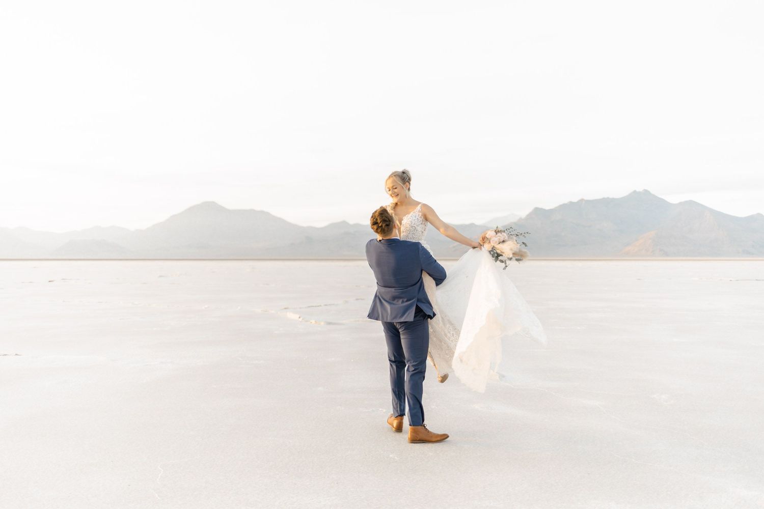 Newlyweds share intimate moments while posing on expansive salt flats with mountain backdrop.