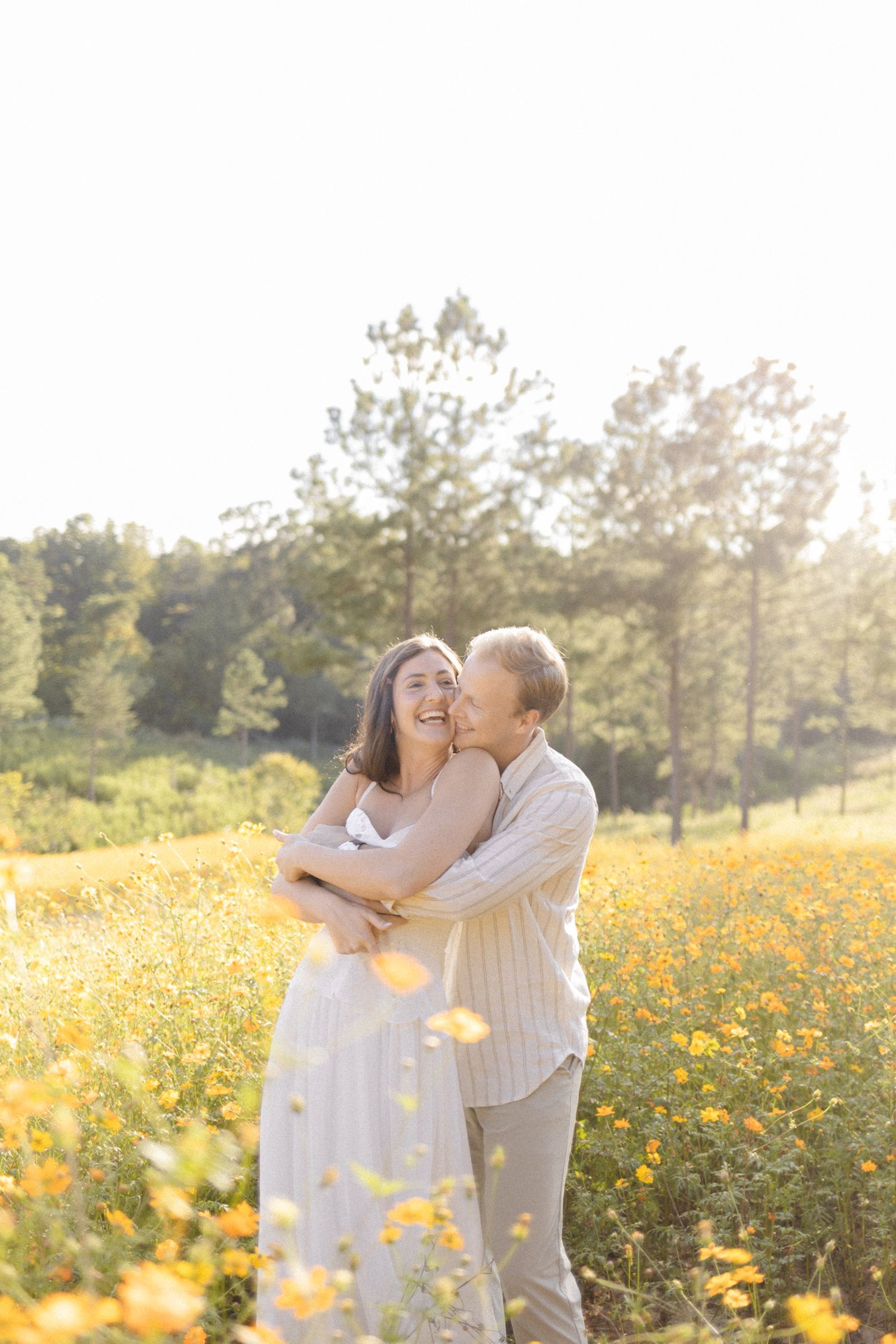 Couple embracing in a golden field of wildflowers during sunset with pine trees in background during lifestyle portrait photoshoot.