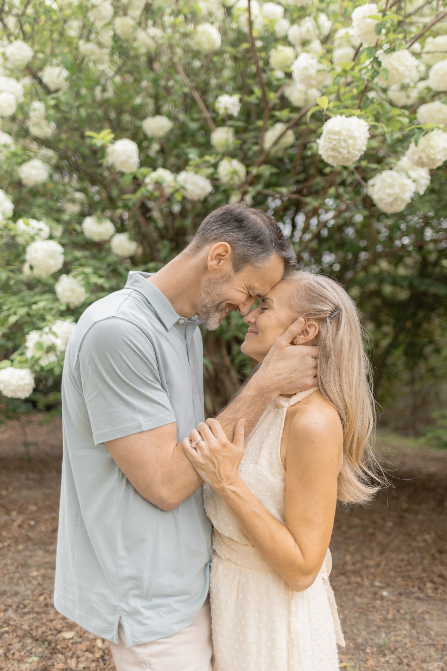 A romantic couple shares an intimate moment in front of blooming white hydrangea bushes in a garden setting.