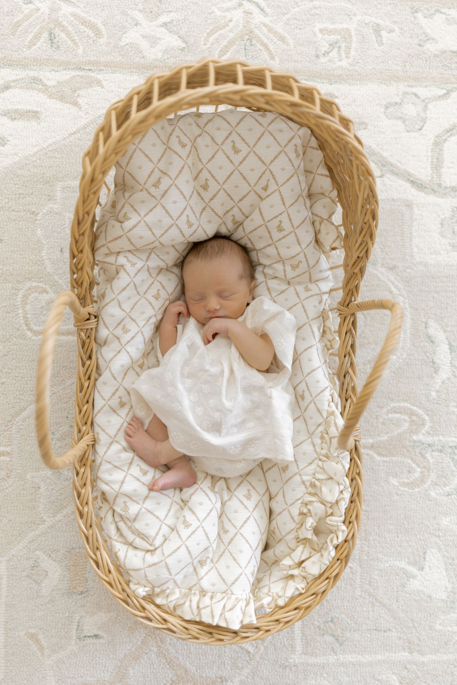 Sleeping newborn baby in a wicker Moses basket with white quilted lining on a cream rug.
