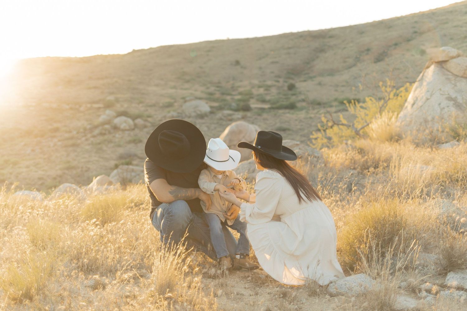 Family in cowboy hats sitting together in golden desert landscape during sunset.