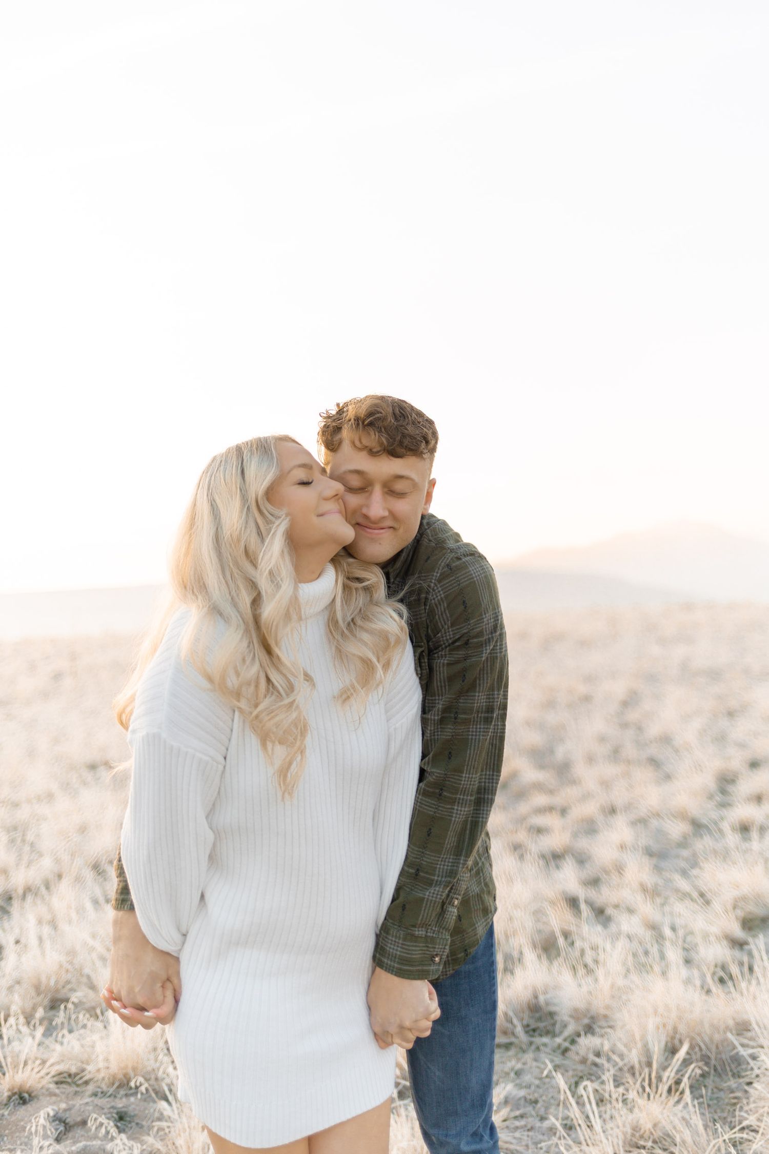 Couple sharing a romantic moment in a golden field, woman in white sweater dress, man in green flannel shirt.