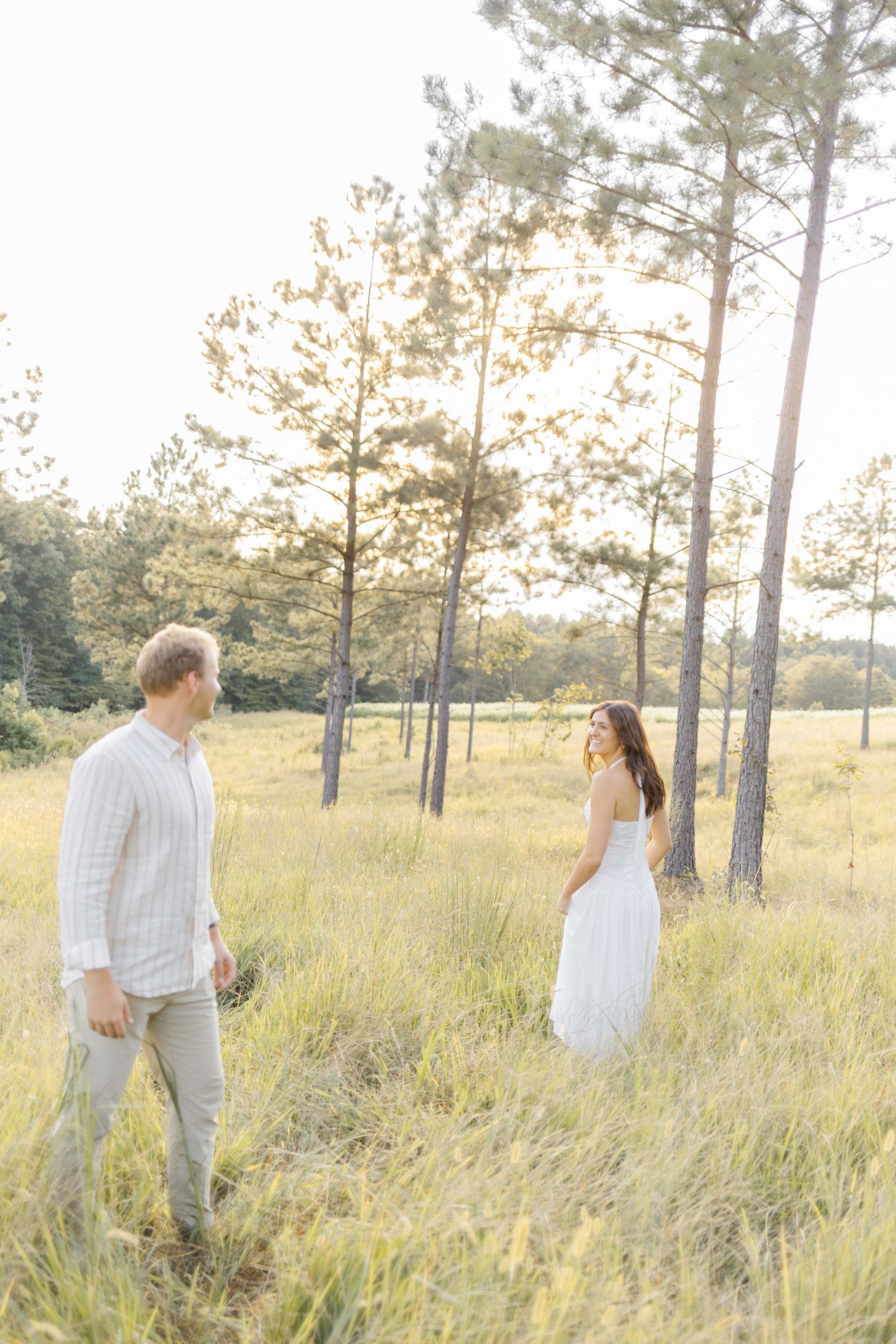 Romantic couple strolling through a serene field with scattered pine trees during sunset during lifestyle portrait photoshoot.