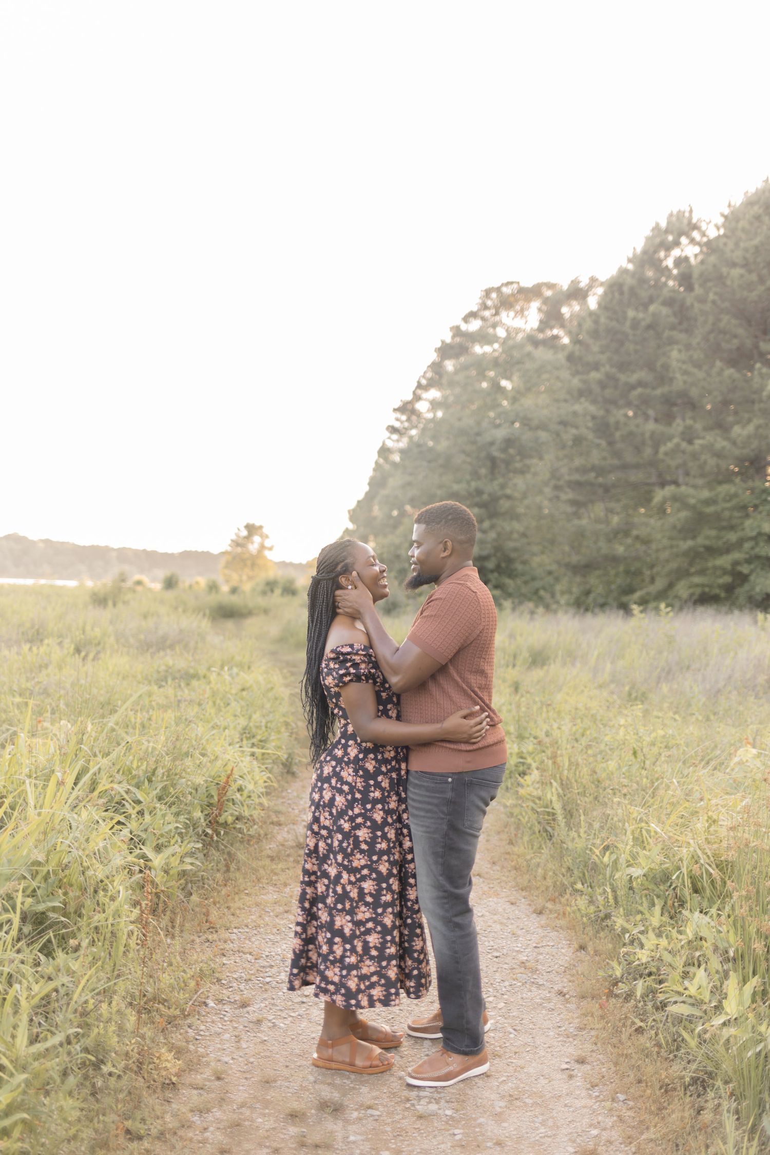 A couple faces each other lovingly on a dirt path surrounded by tall grass during golden hour.