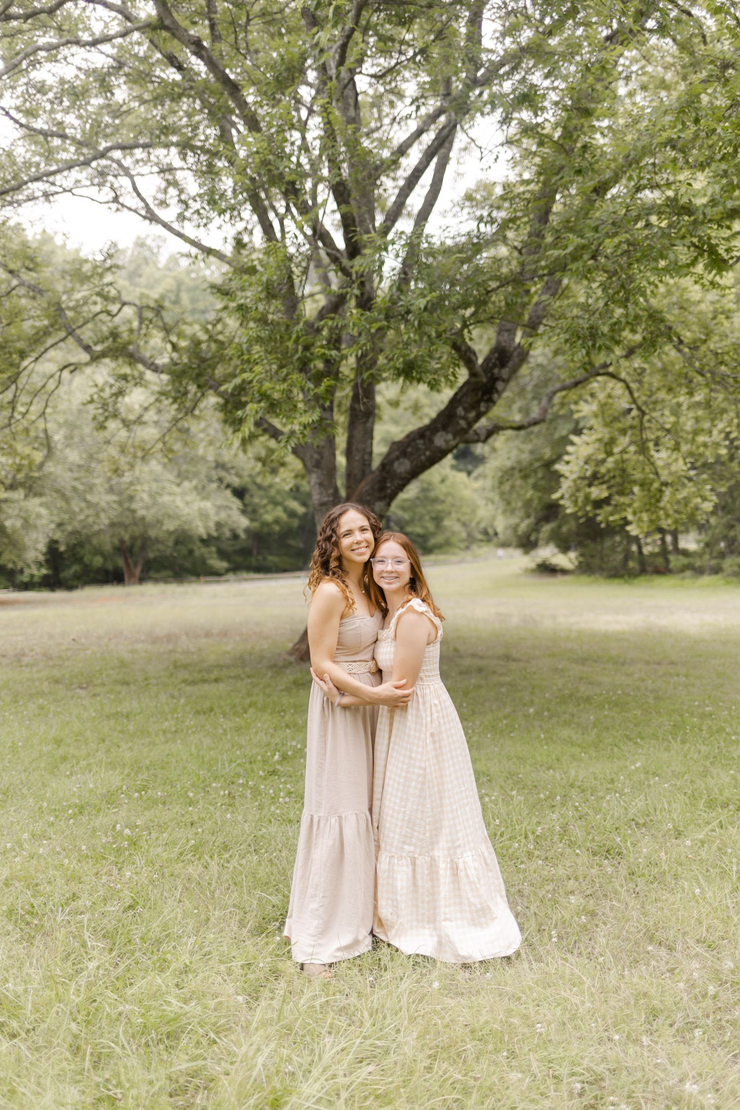 Two people in matching cream dresses embrace while standing in a peaceful park setting in Durham, North Carolina.