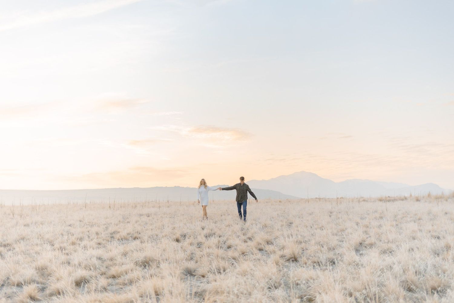 Two people walking hand in hand across a misty desert plain at sunrise at photoshoot in Antelope Island, Utah