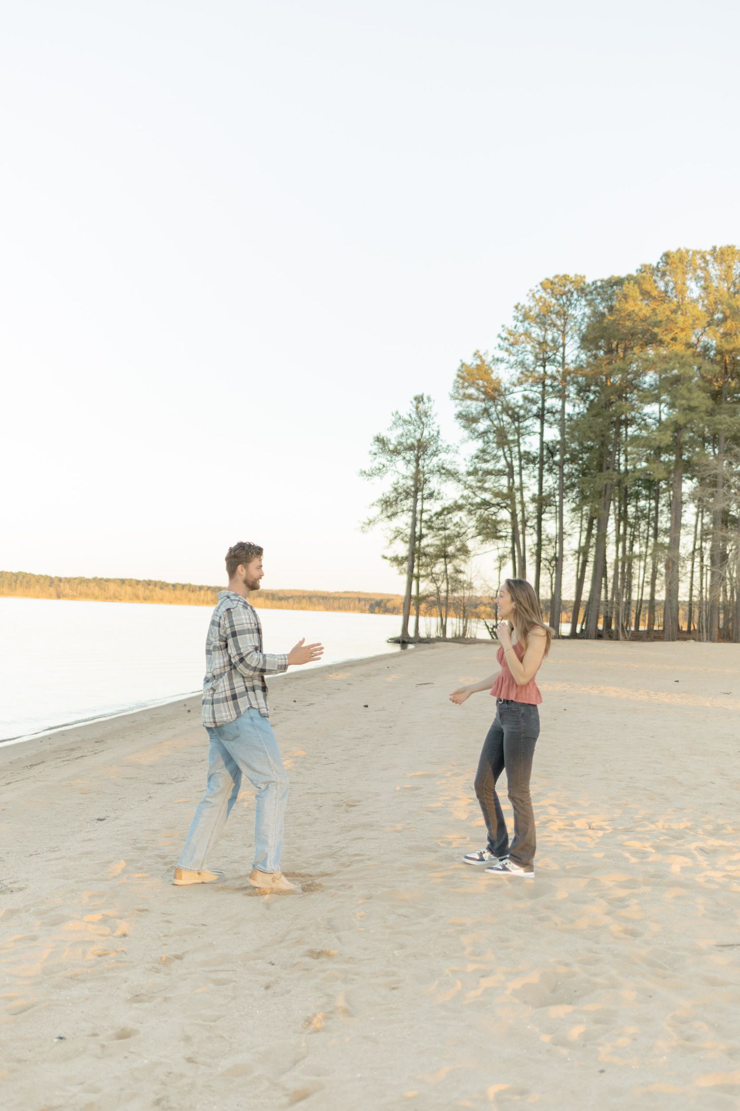 Couple walking and playing on sandy dunes with pine trees in the background in Raleigh, North Carolina.