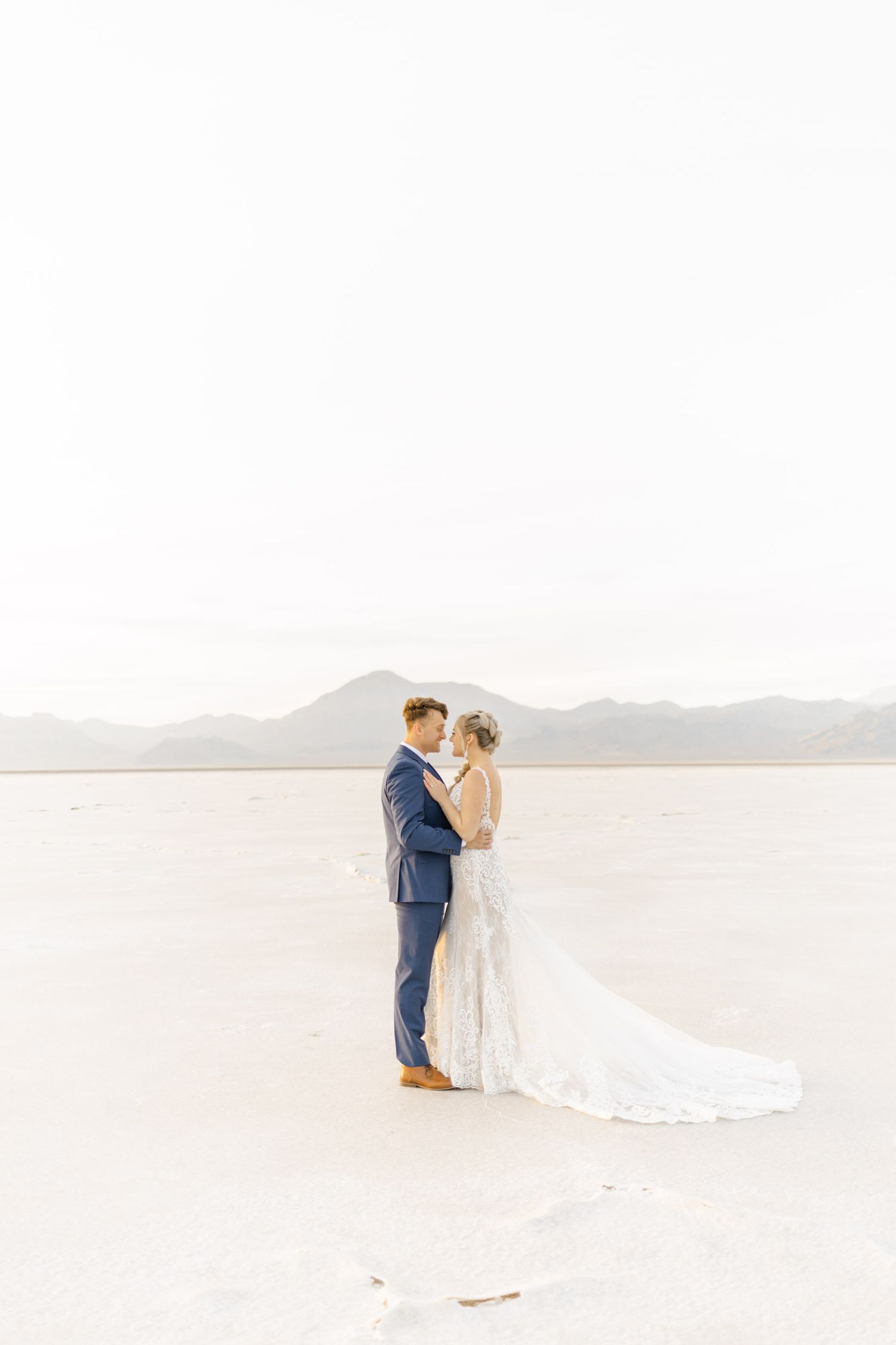 Wedding couple shares an intimate moment on bright desert salt flats with mountain views.
