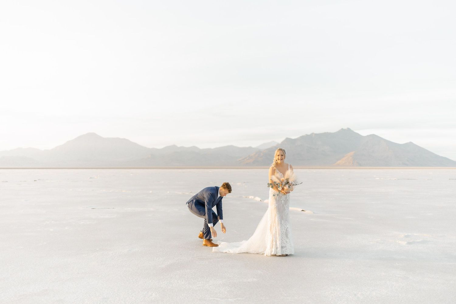 Two people stand on the stark white salt flats with mountains in the background during a photo session.