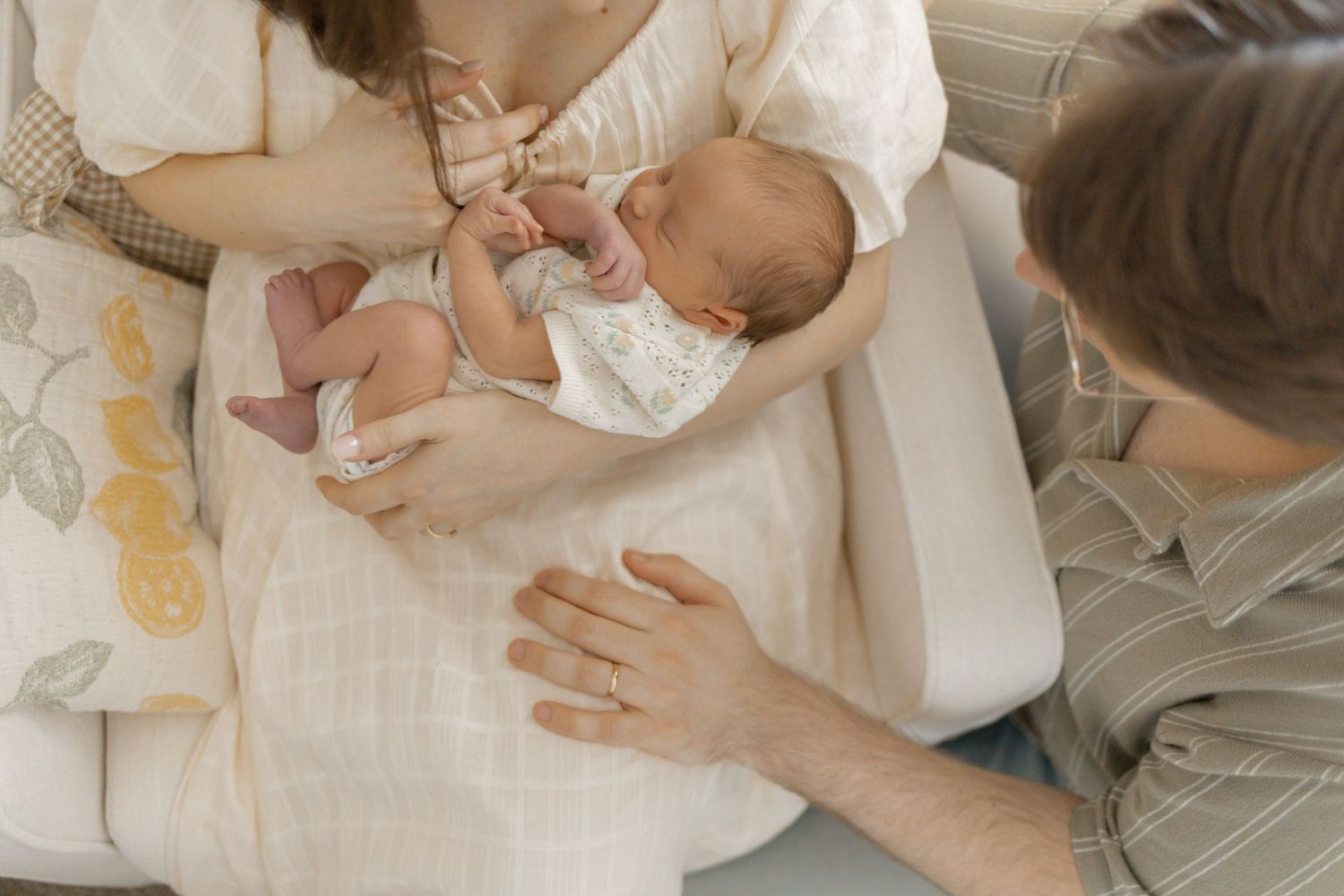 Mother cradling newborn baby while father gently touches infant during peaceful family moment at home.