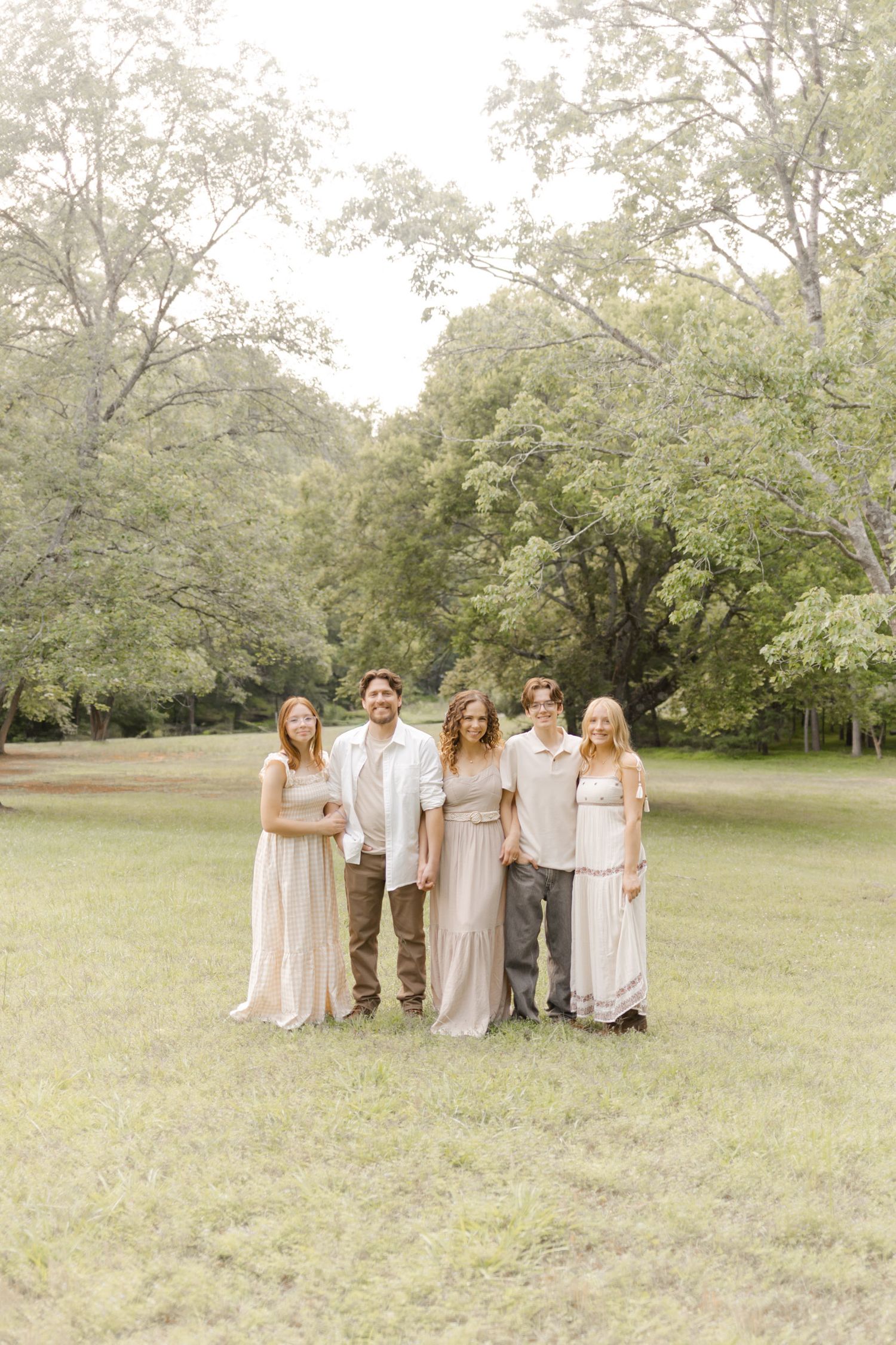 Group portrait of friends in neutral colored outfits standing together in a grassy field.