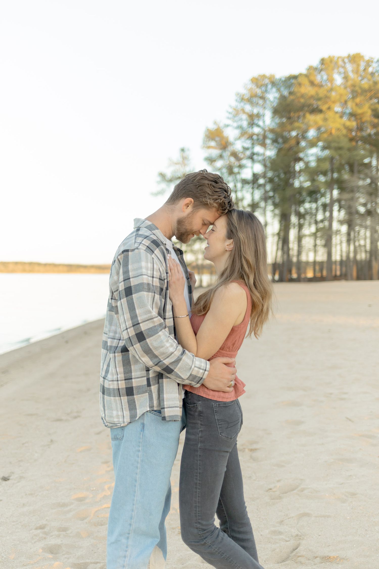 Couple in casual attire sharing an intimate moment on a sandy hillside with trees behind them in Raleigh, North Carolina.