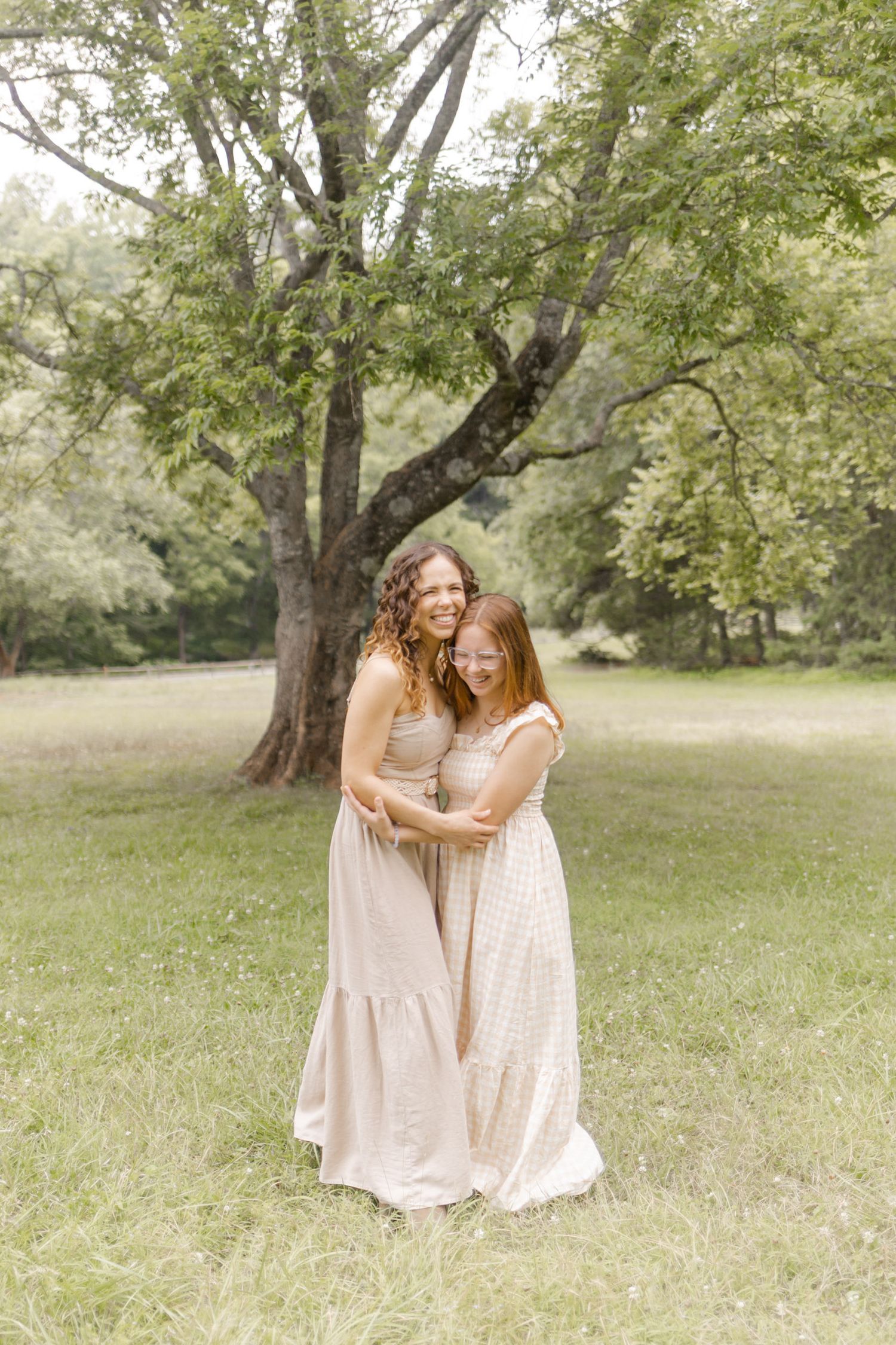 Two people in light summer dresses share an intimate moment in a sunny park setting during photoshoot in Durham, NC.