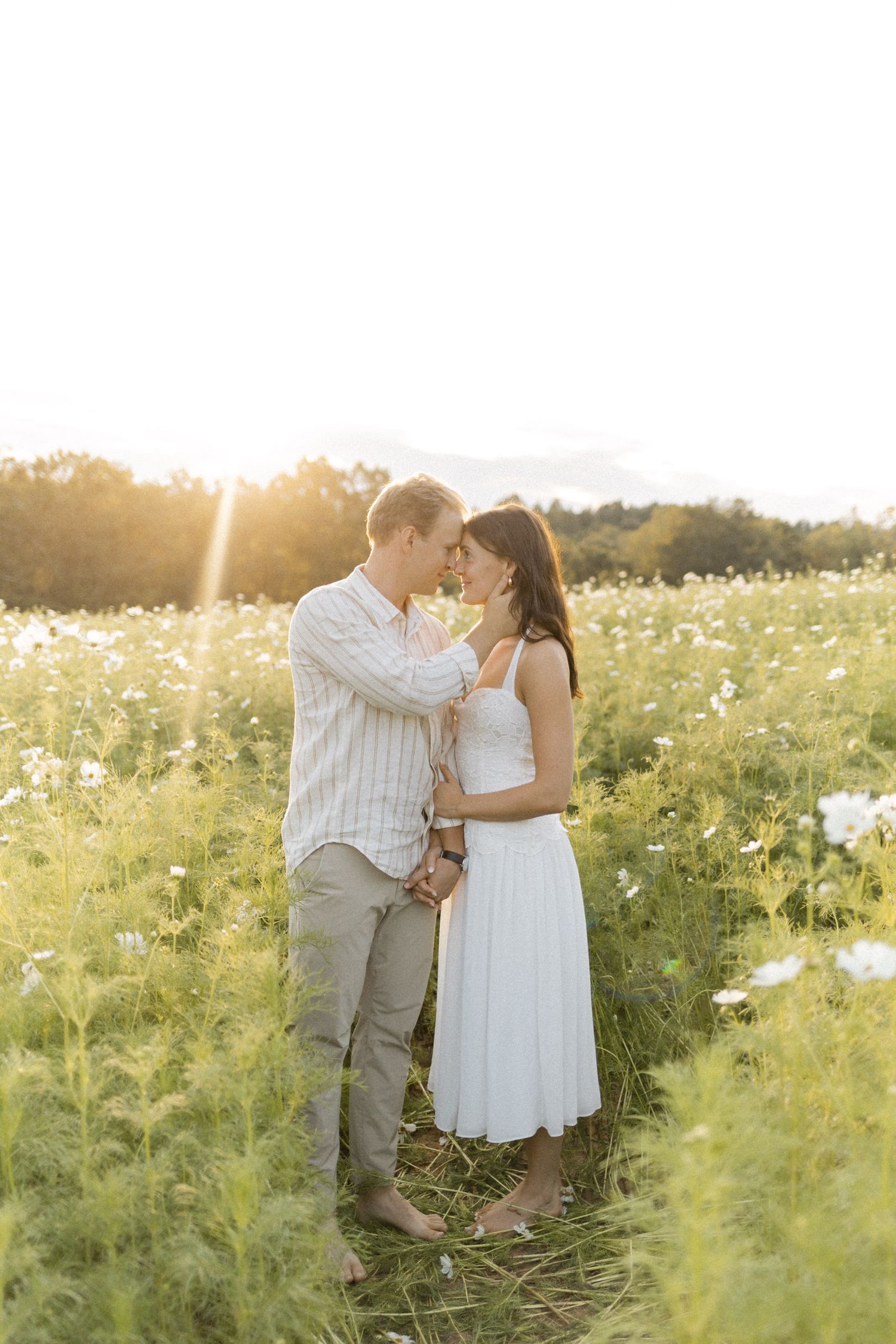 Romantic moment captured in a meadow filled with white and yellow wildflowers during engagement session with photographer in North Carolina.