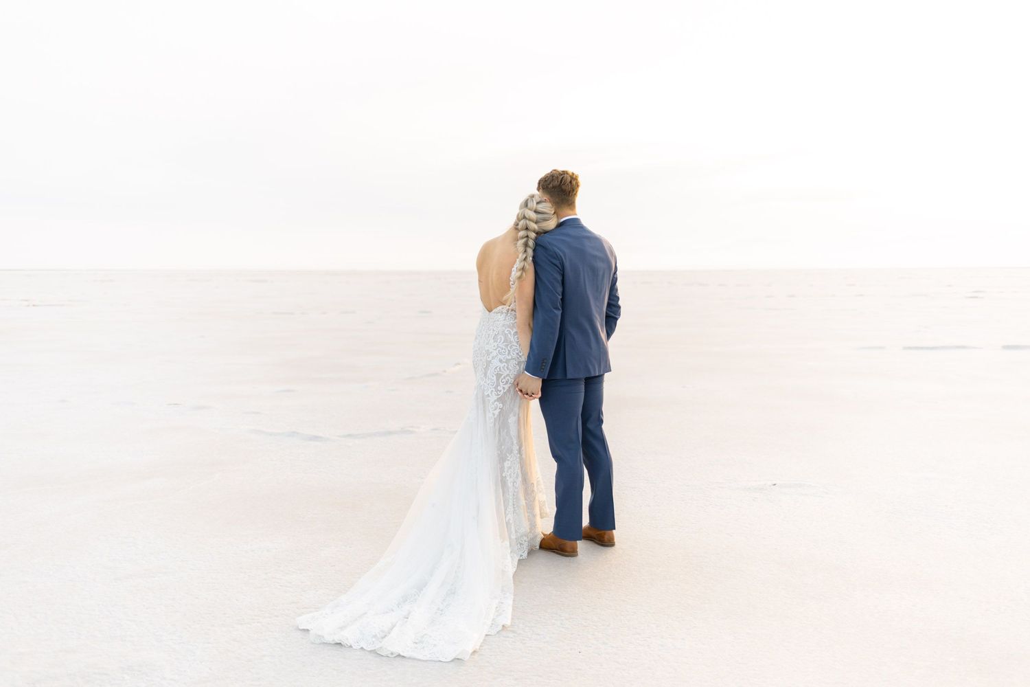 A bride and groom share an intimate moment on a bright white sandy beach at sunset.