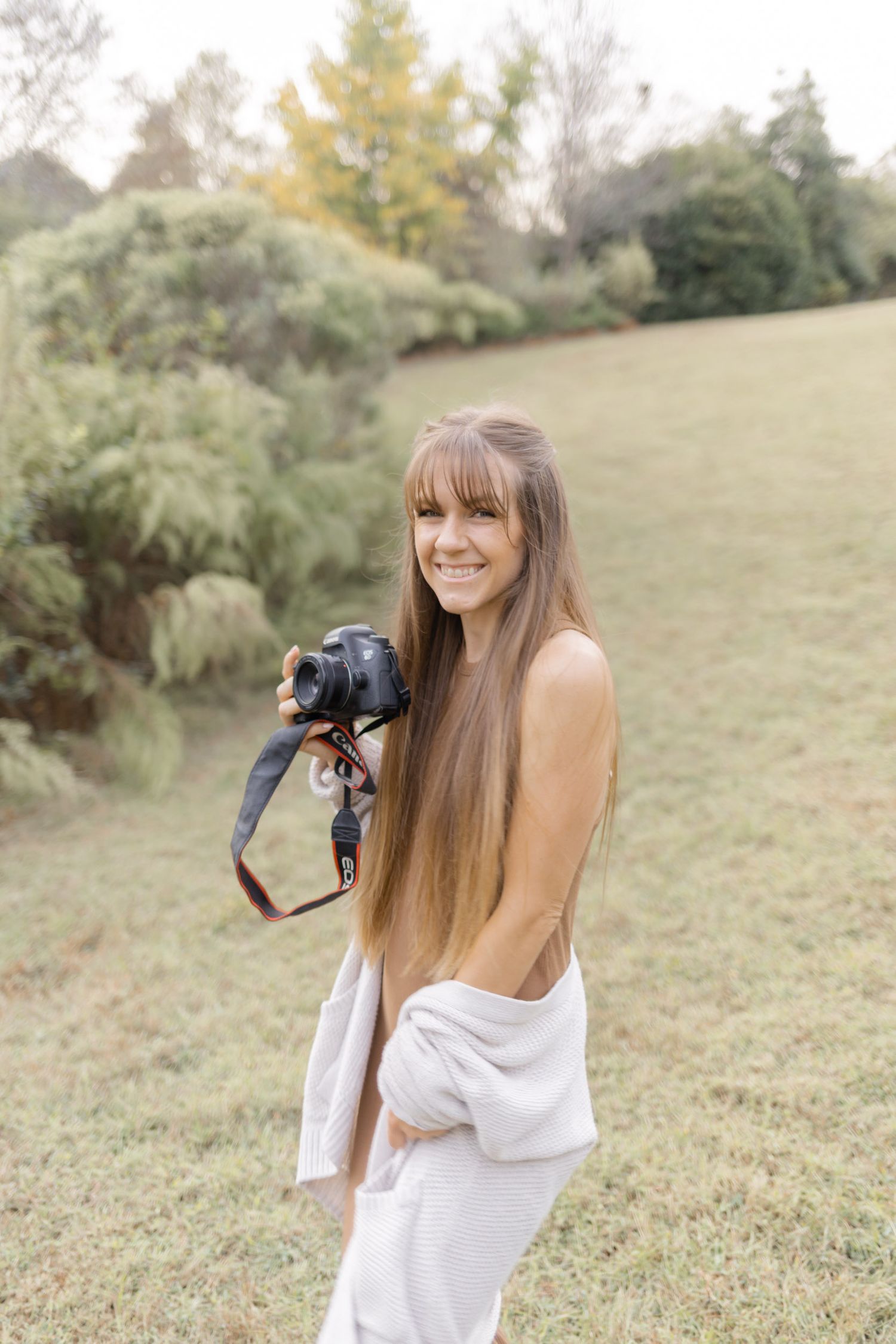 Photographer in white dress takes photos in a sunlit meadow with soft natural lighting.
