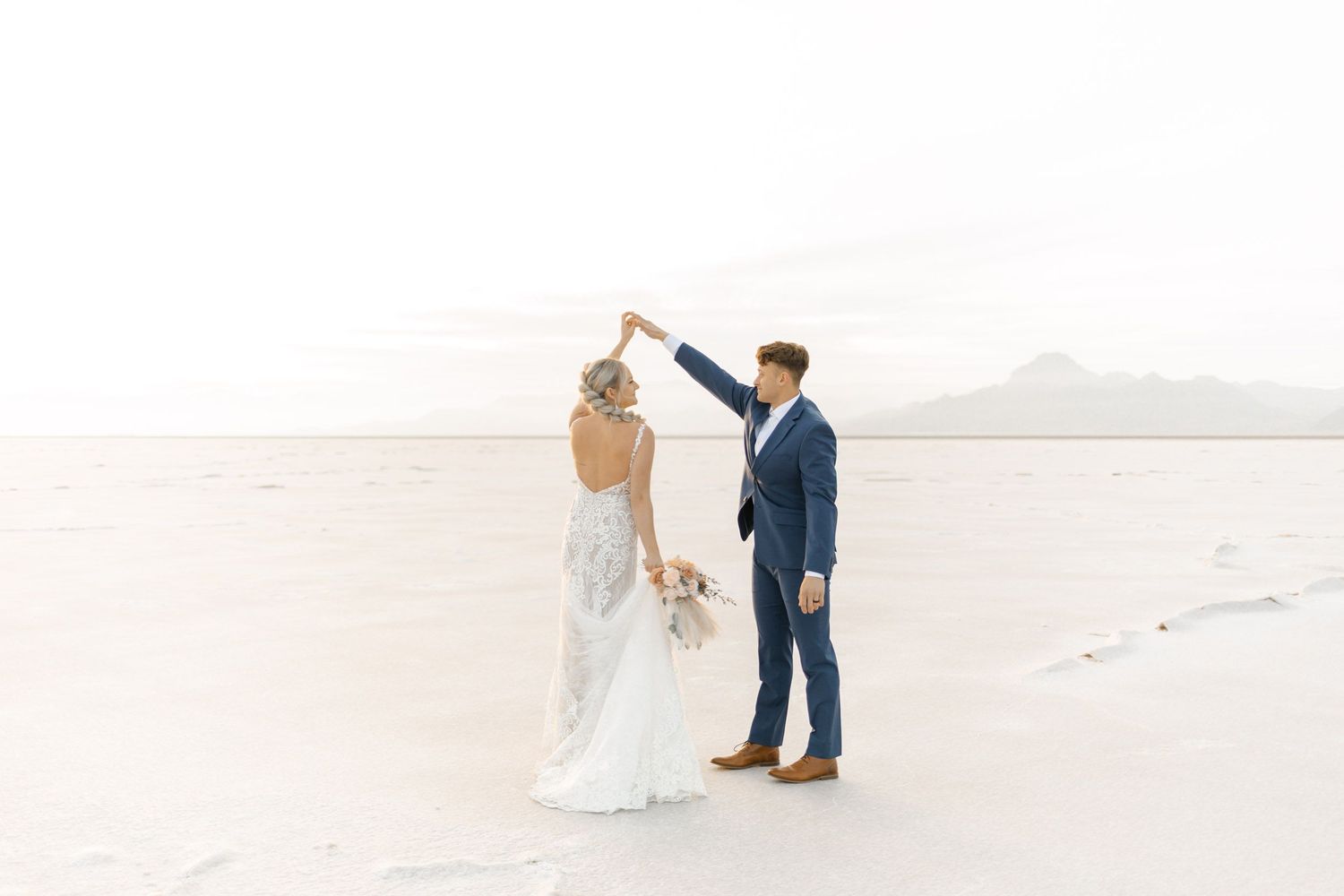 Romantic wedding photos captured on vast white salt flats with mountains on the horizon.