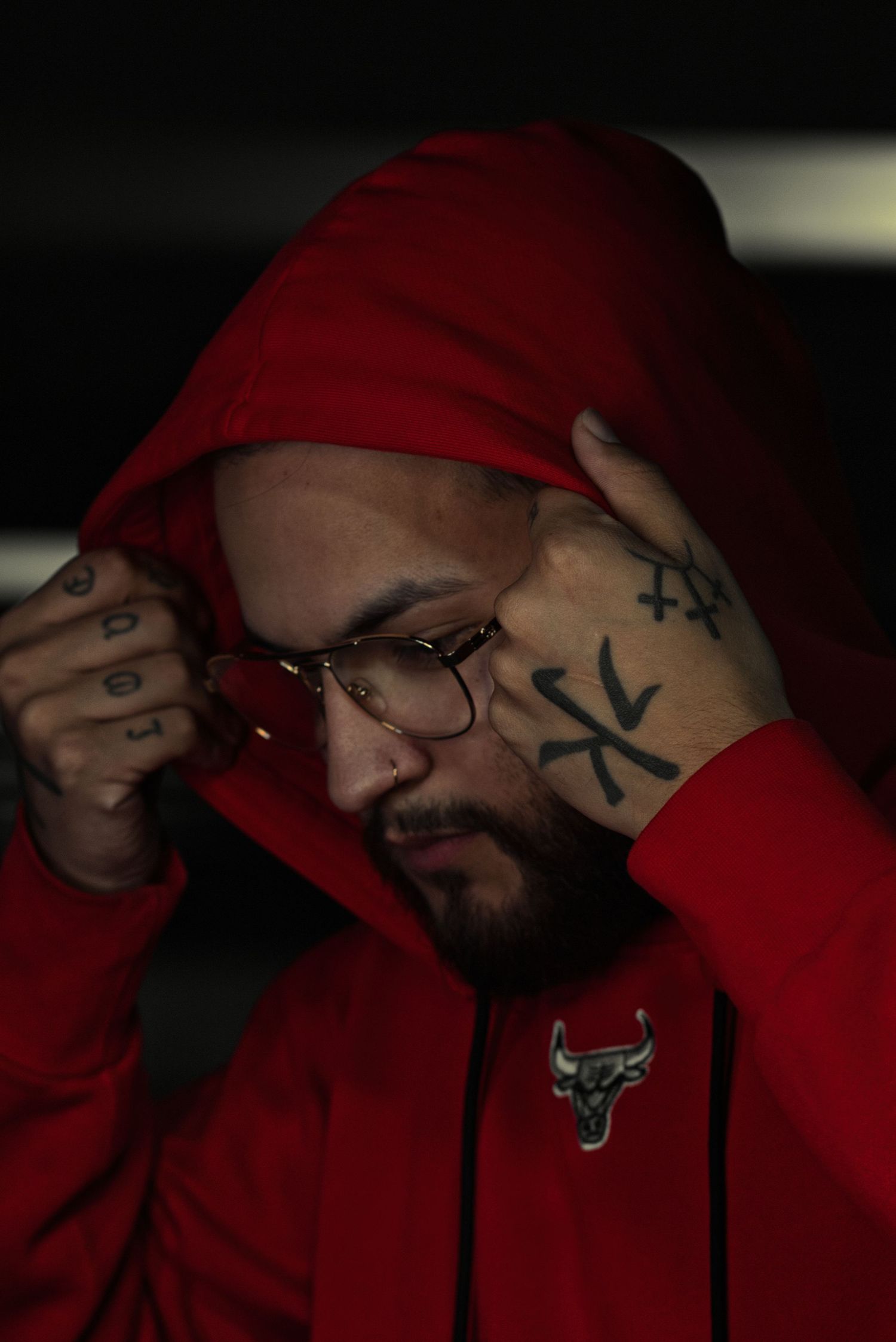 Person wearing a red Chicago Bulls hoodie and glasses in dramatic low-key lighting.