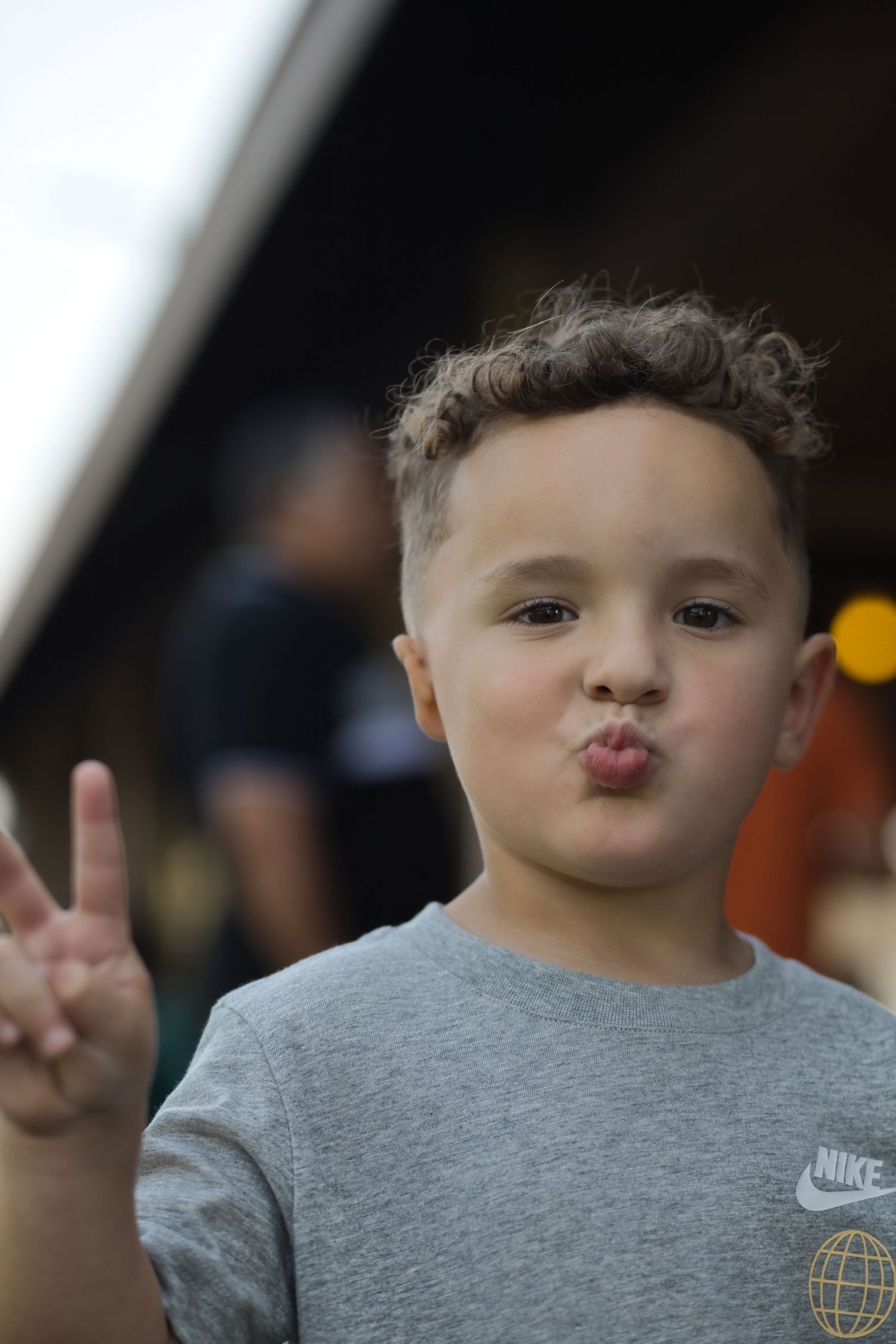 Young child in grey Nike shirt making peace sign and playful expression.