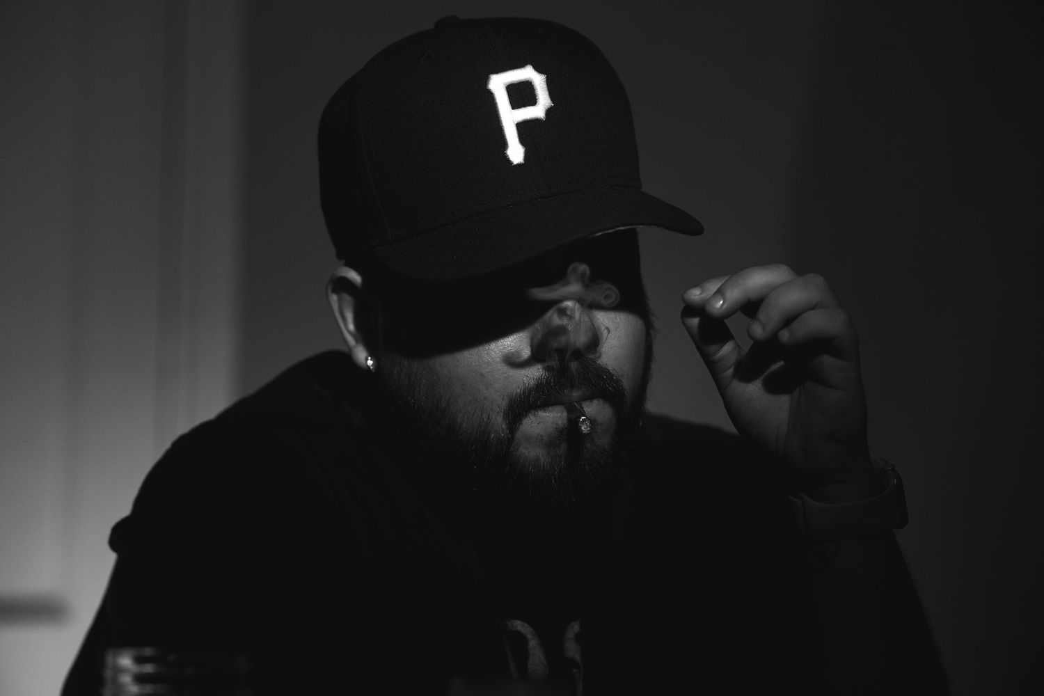 Black and white photo of a man in a Pittsburgh Pirates cap smoking a cigar in dramatic lighting.
