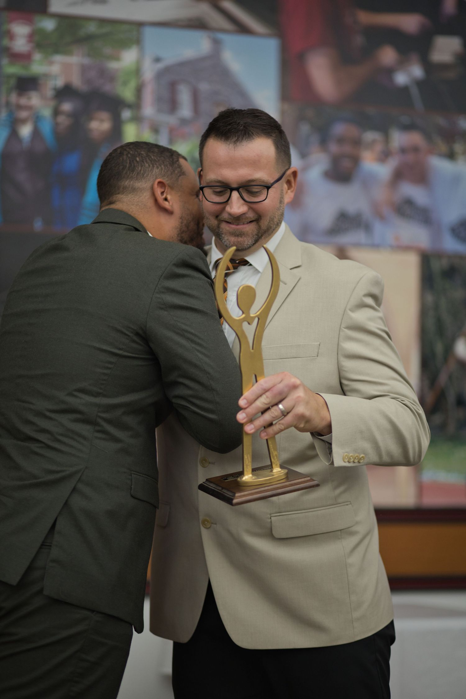 Two men in suits share an emotional moment at what appears to be an awards ceremony.