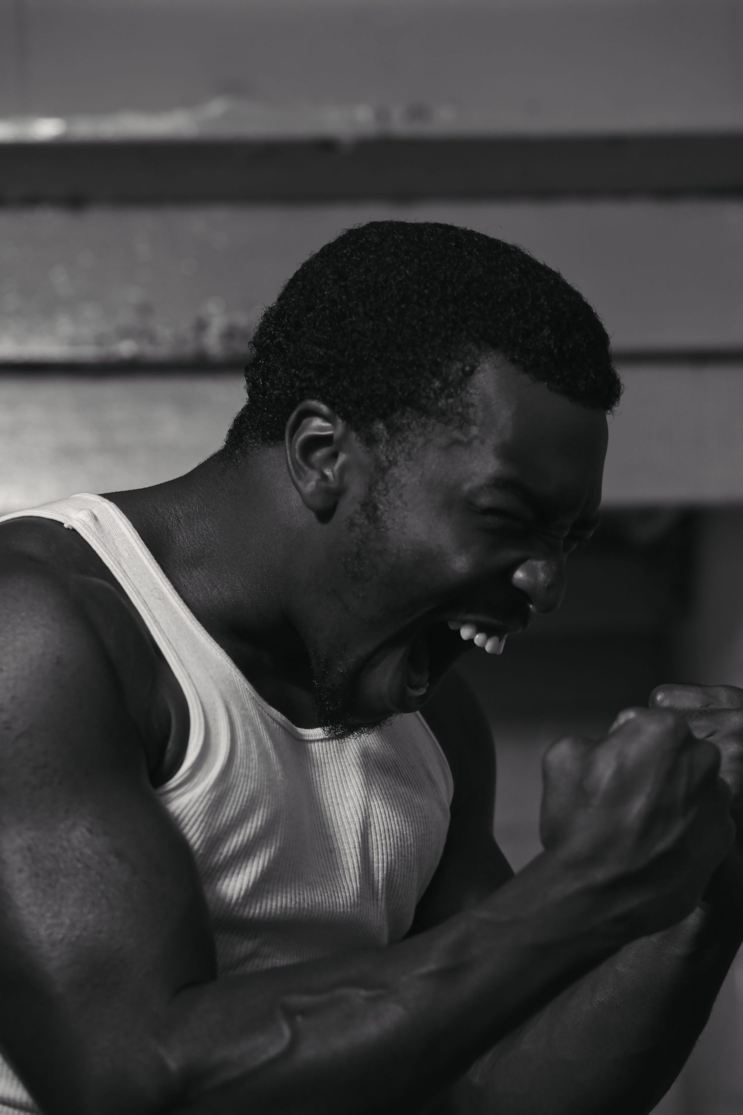 Man in white tank top laughing and showing emotion in dramatic black and white portrait.