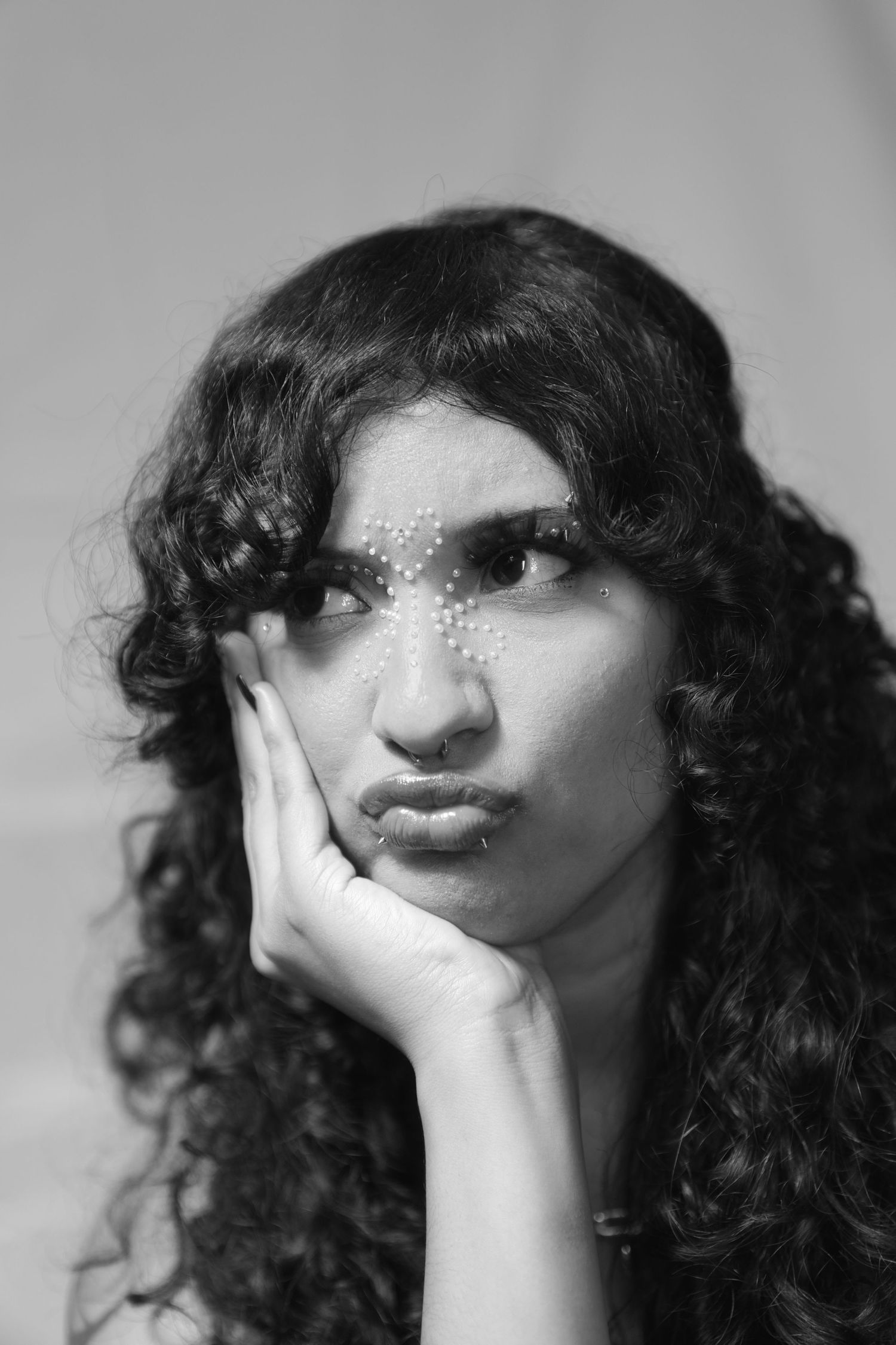 Black and white portrait of a young woman with curly hair resting her chin on her hand, looking thoughtful.